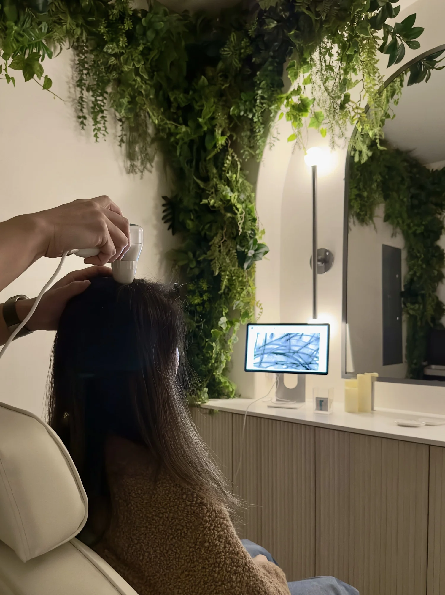 Client in a treatment chair beside a green plant wall and scalp analysis screen at Cosh Head Spa