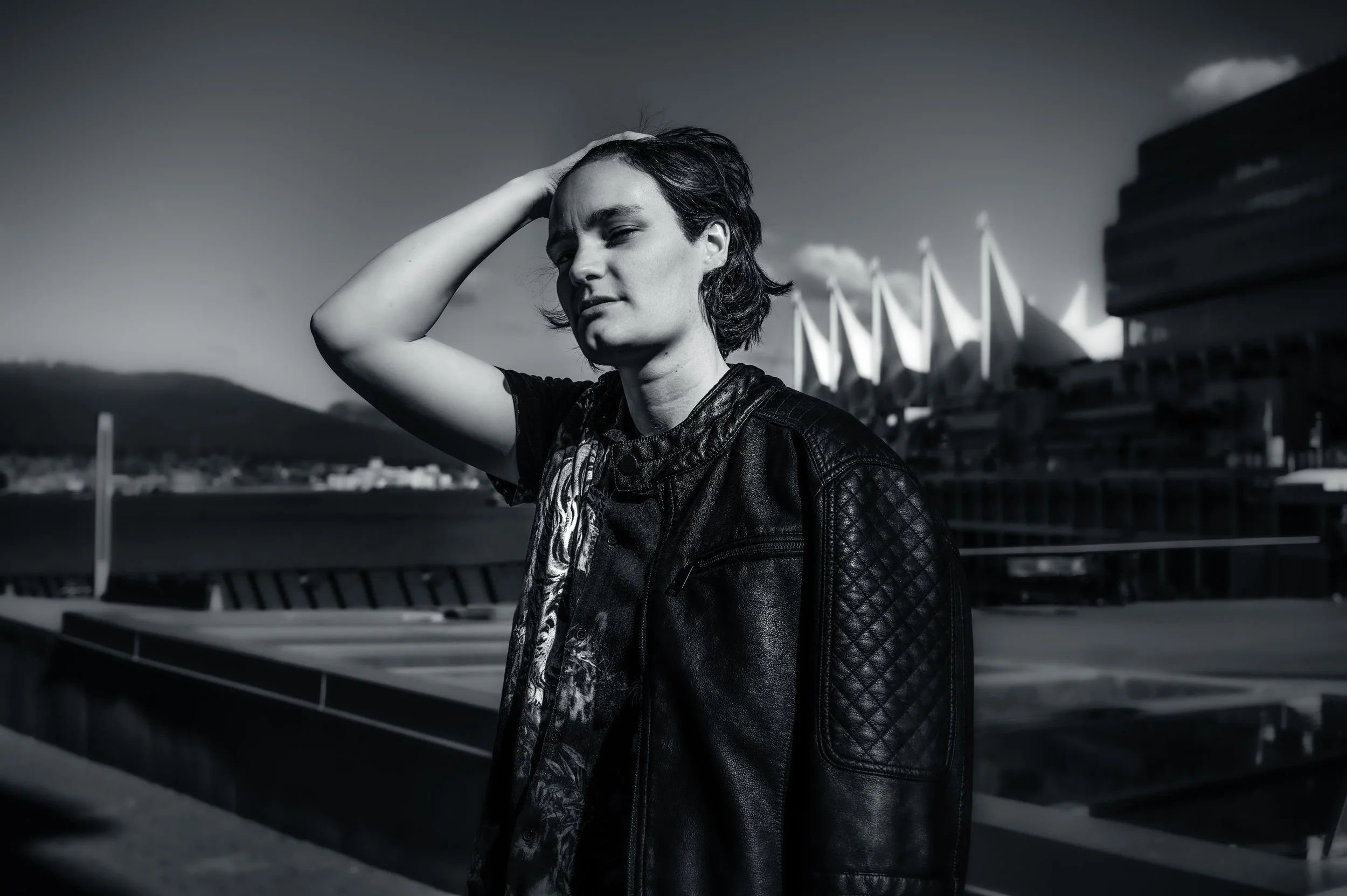 Portrait de Sara Hoskins, créatrice de jeux vidéos à Vancouver avec les cheveux longs, portant une veste en cuir, se tient devant le bâtiment de l'Opéra de Sydney sous un ciel nuageux.