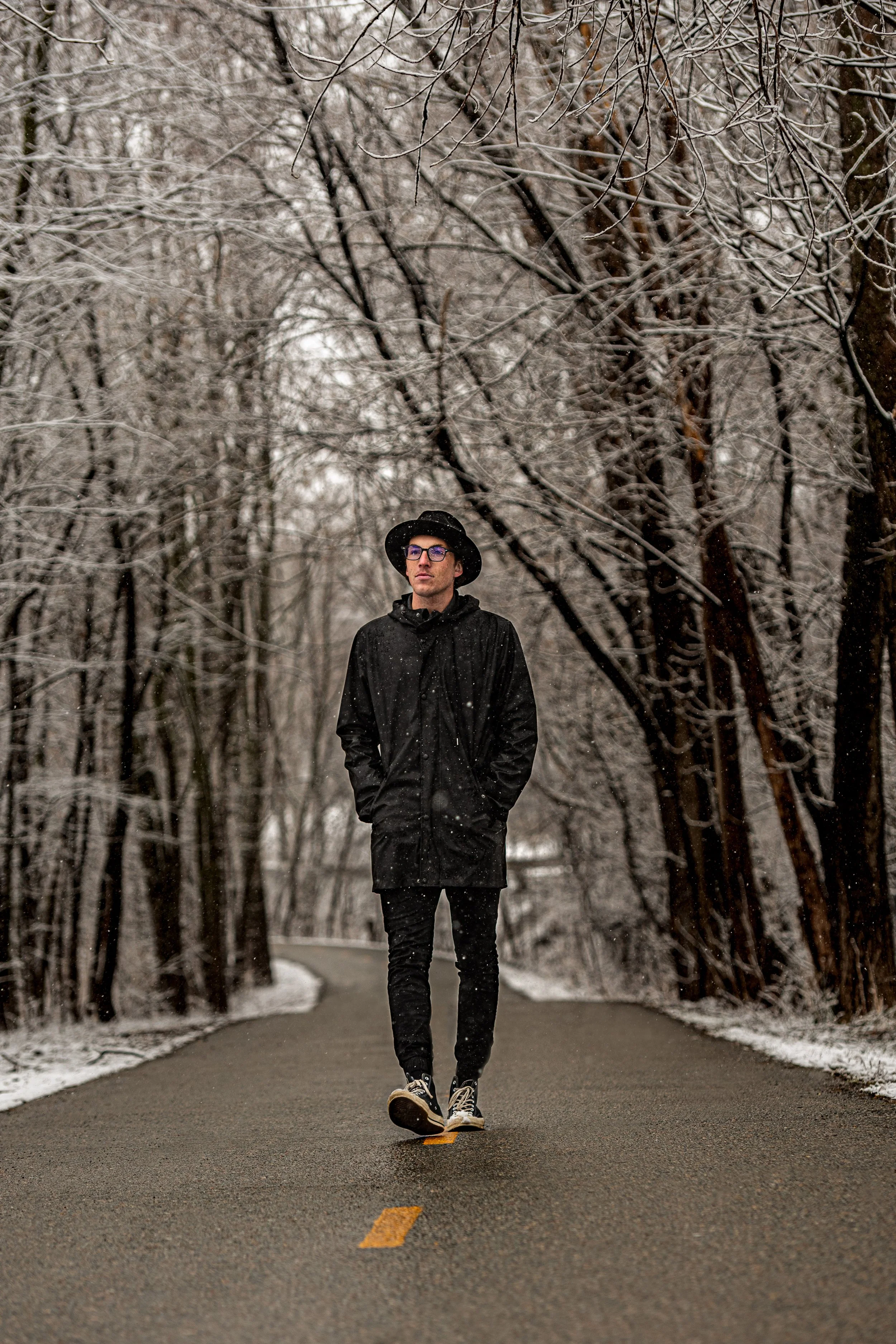 Portrait de Thomas Windisch, auteur, portant un manteau noir, un chapeau noir et des lunettes, fumant une cigarette dans un tunnel métallique sous une tempête de neige à Sherbrooke au Québec.
