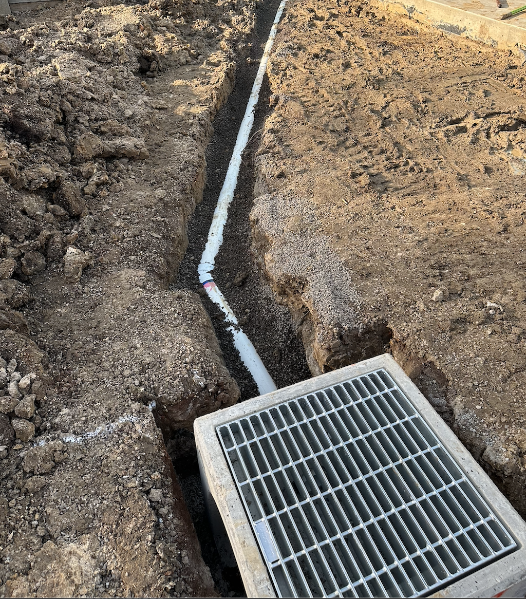 Trench with drainage pipe, pit, and grate lid.