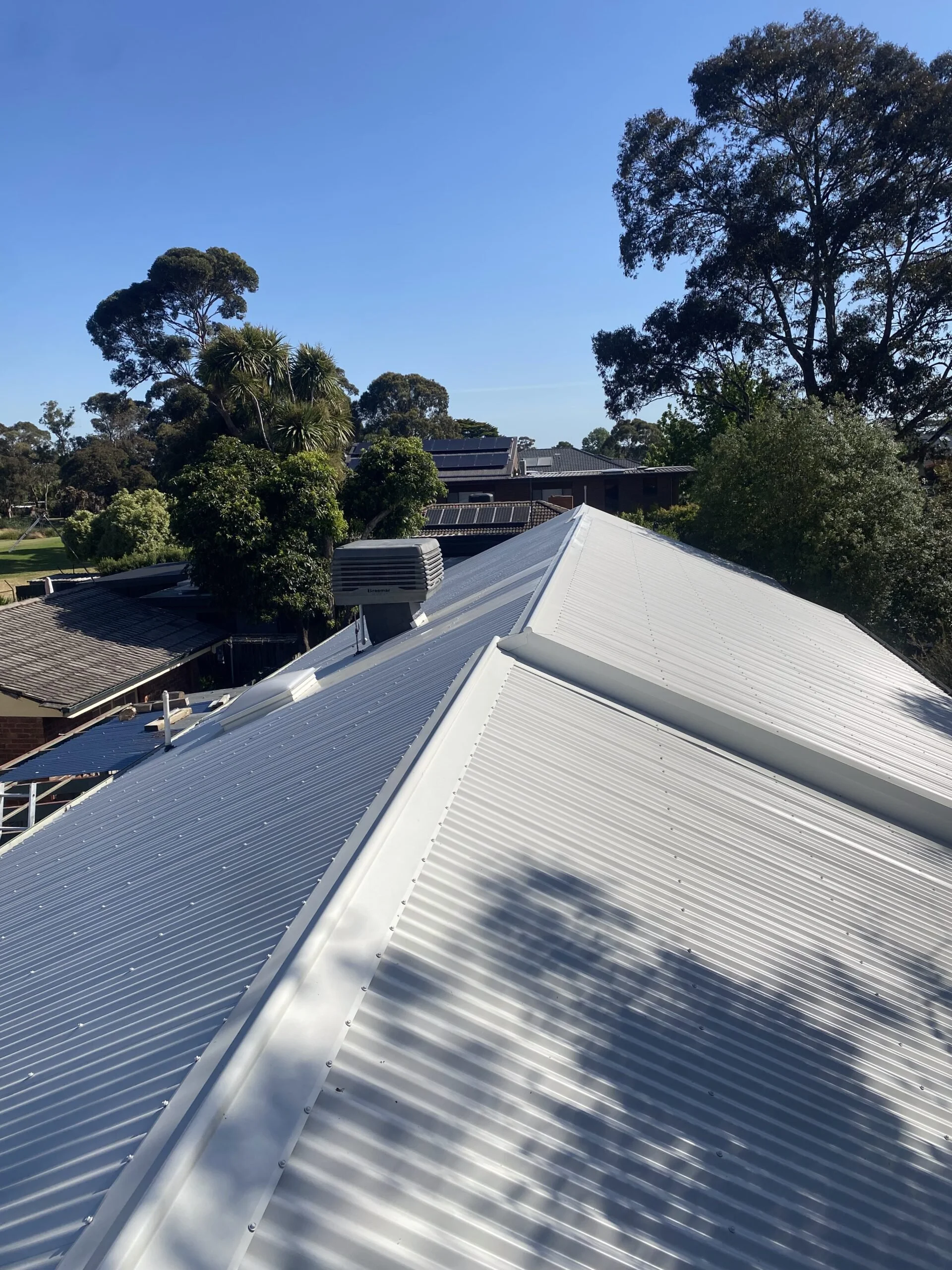 Corrugated metal roof with trees in the background under a clear blue sky.