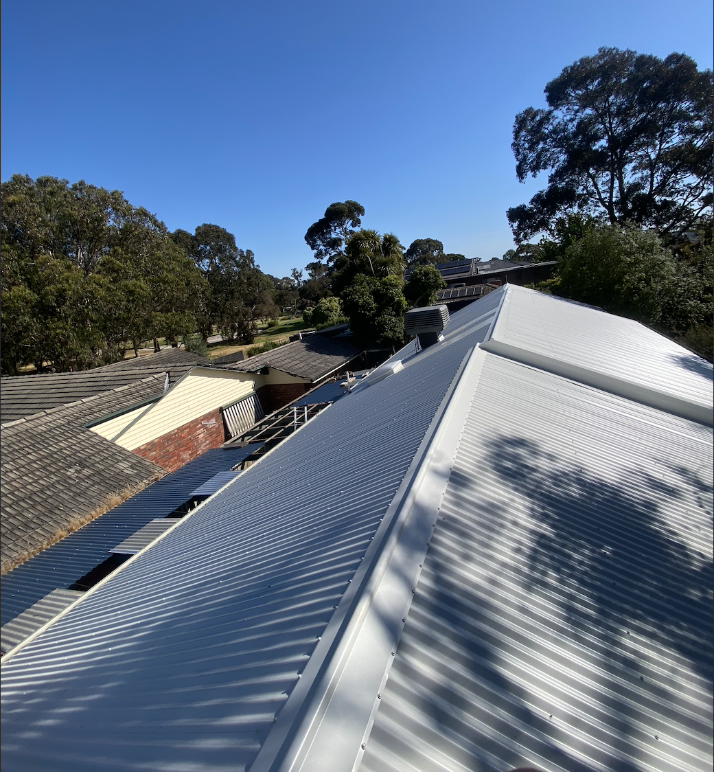 View of a corrugated metal roof with trees and a clear blue sky in the background.