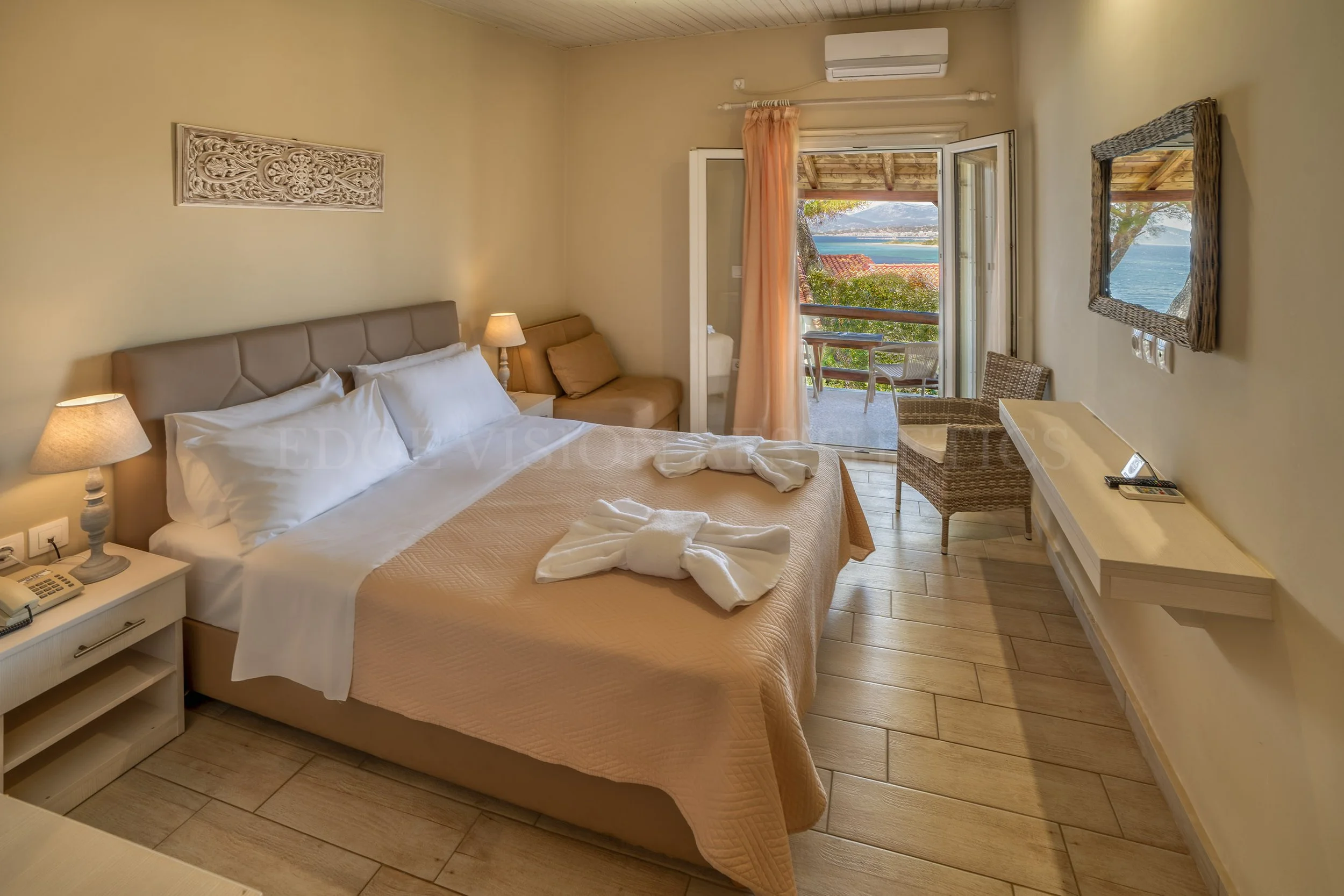 A hotel room with a large bed, nightstand, lamps, and a balcony with ocean view.