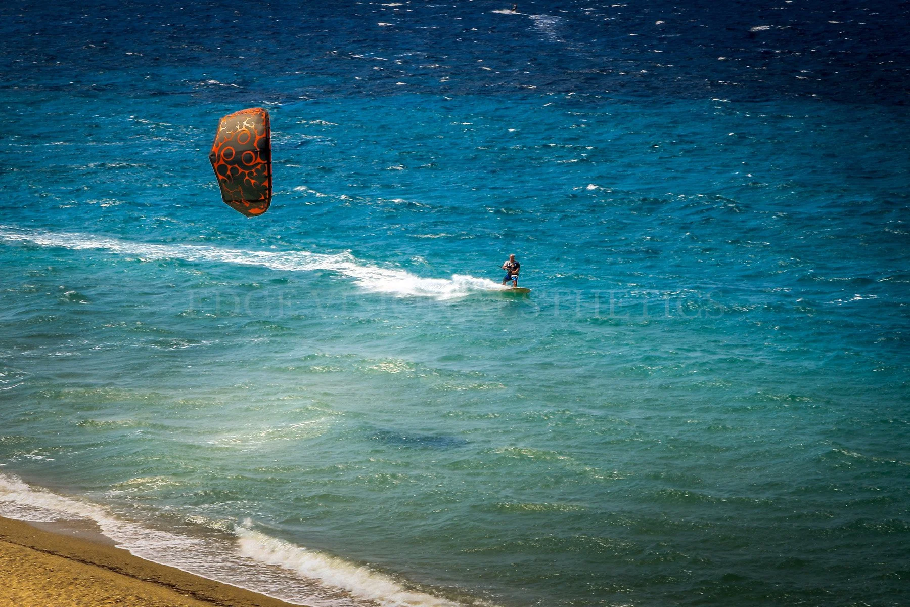 A person kiteboarding on ocean waves near the sandy beach.