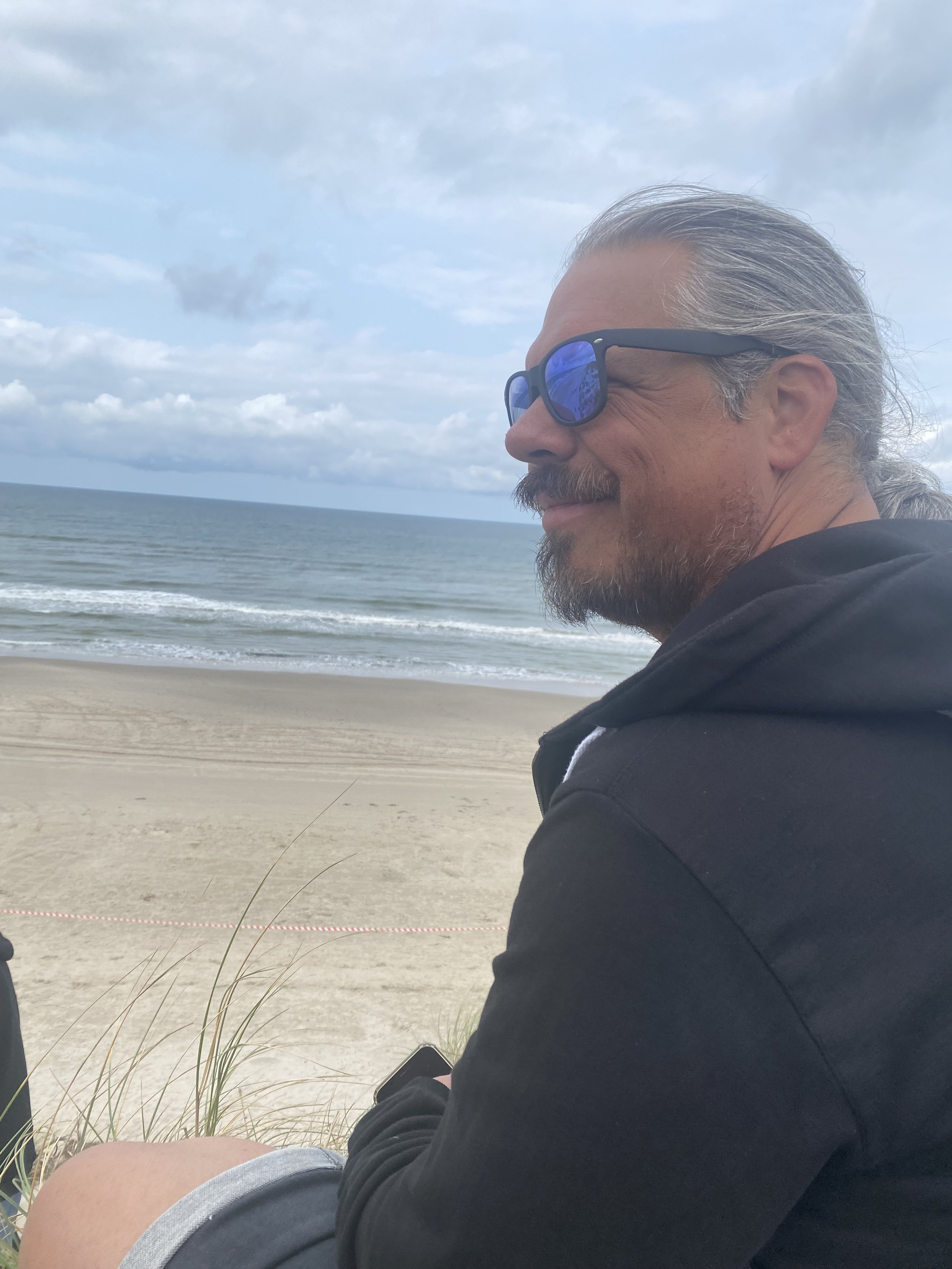 Ein Mann mit Sonnenbrille sitzt am Strand und schaut aufs Meer.