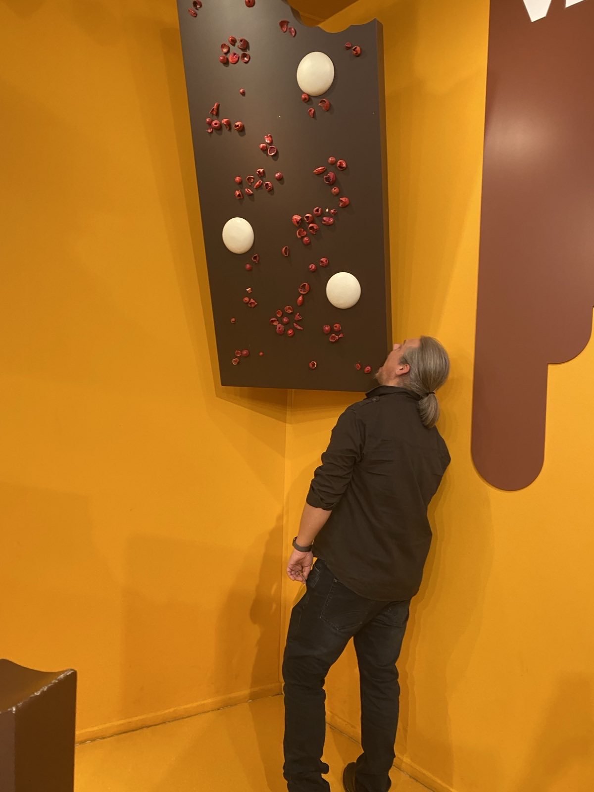 Mann steht vor einer übergroßen Schokoladentafel-Wand, die in Lego-Stil dekoriert ist, mit gelbem Hintergrund.