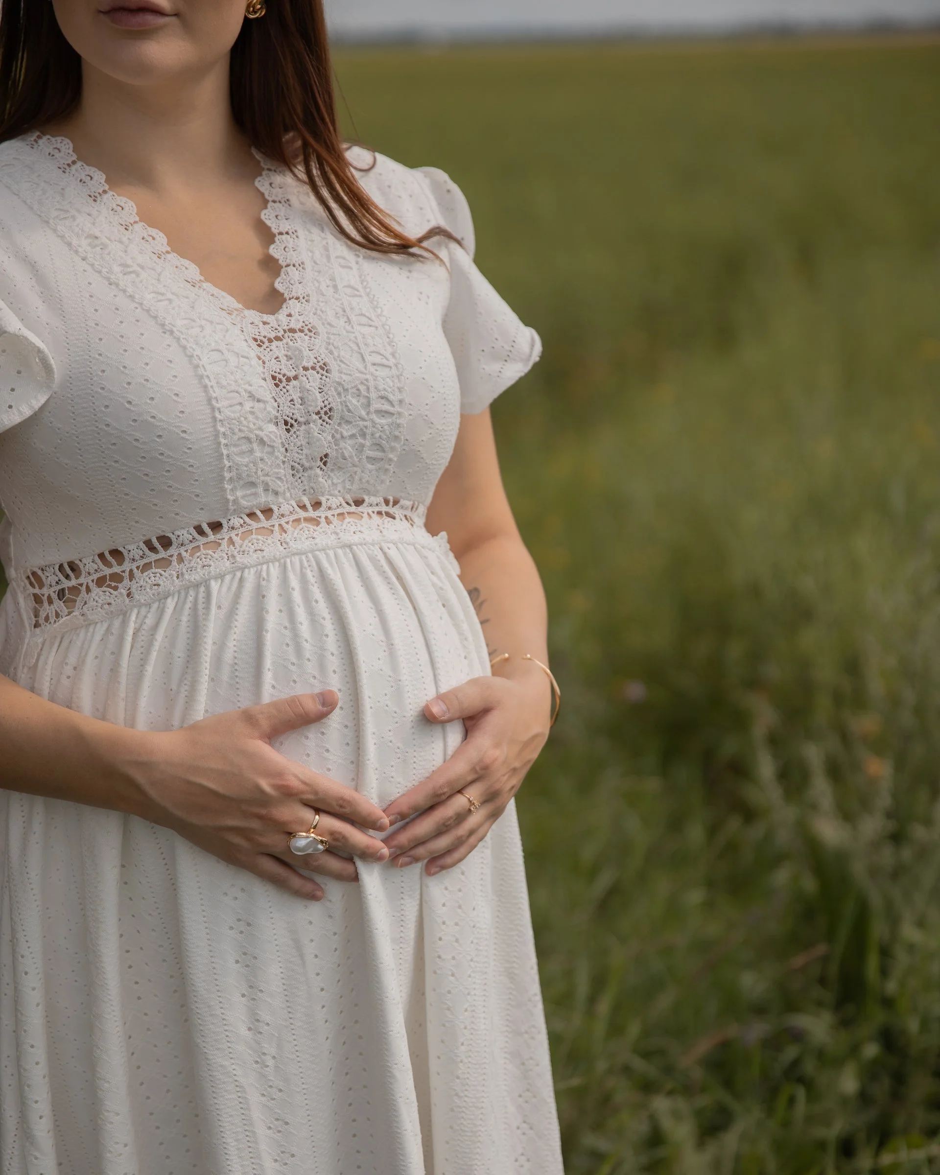 Raskaana oleva nainen, joka pitää käsiä vatsansa päällä ulkona vihreällä niityllä.