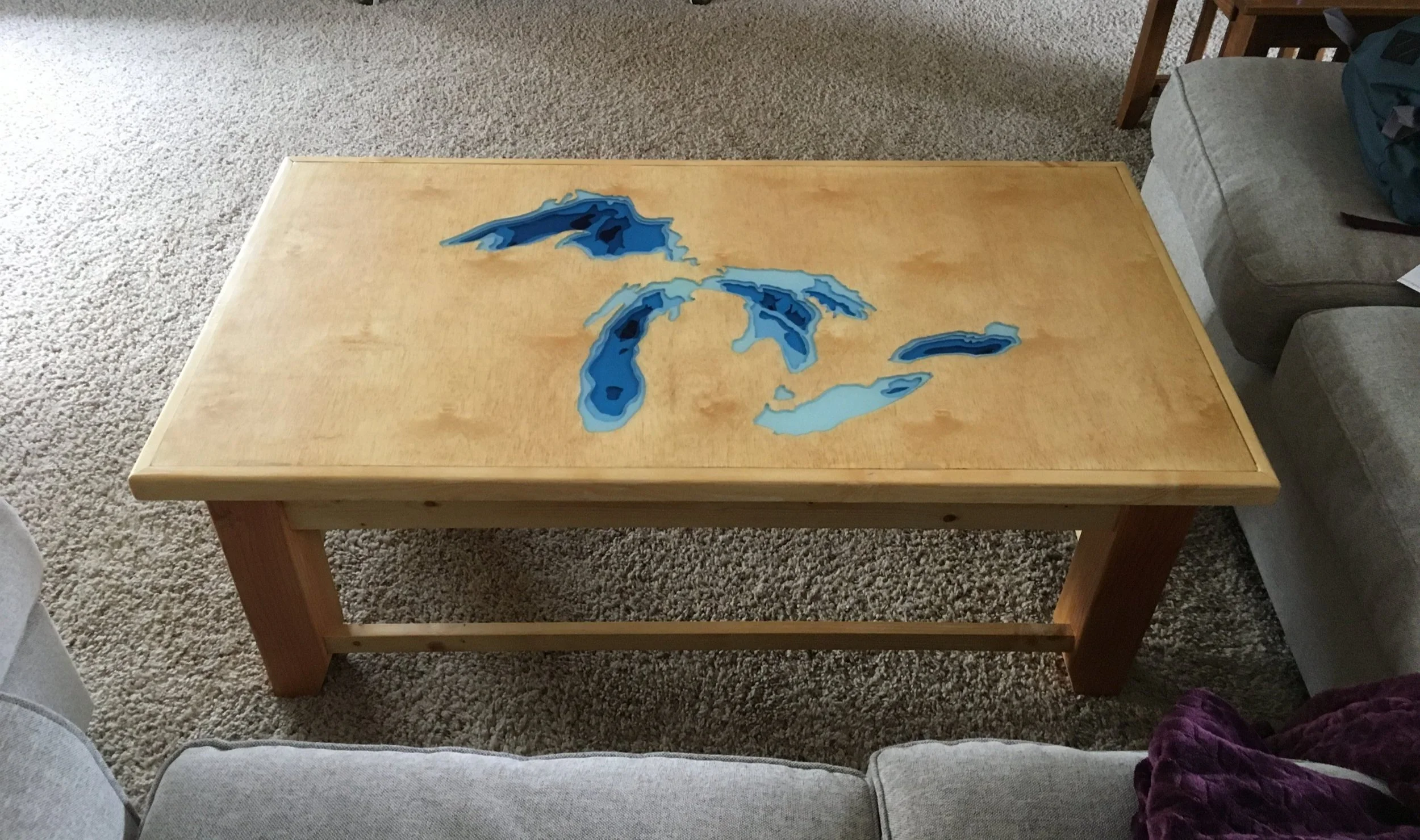 Wooden coffee table with a topographic map of the Great Lakes on the surface, situated in a living room setting.