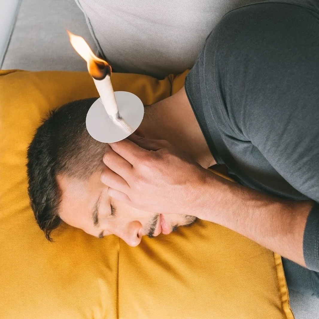 Person lying on a yellow cushion using an ear candle, with a flame at the end of the candle.