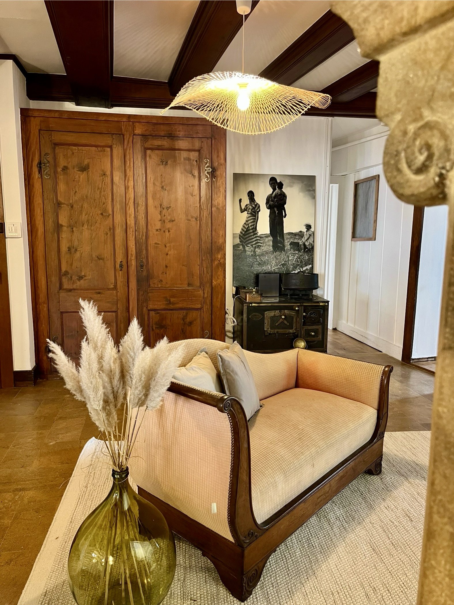 Salon avec canapé en bois, vase avec des pampas, télévision ancienne, tableau noir et porte en bois.