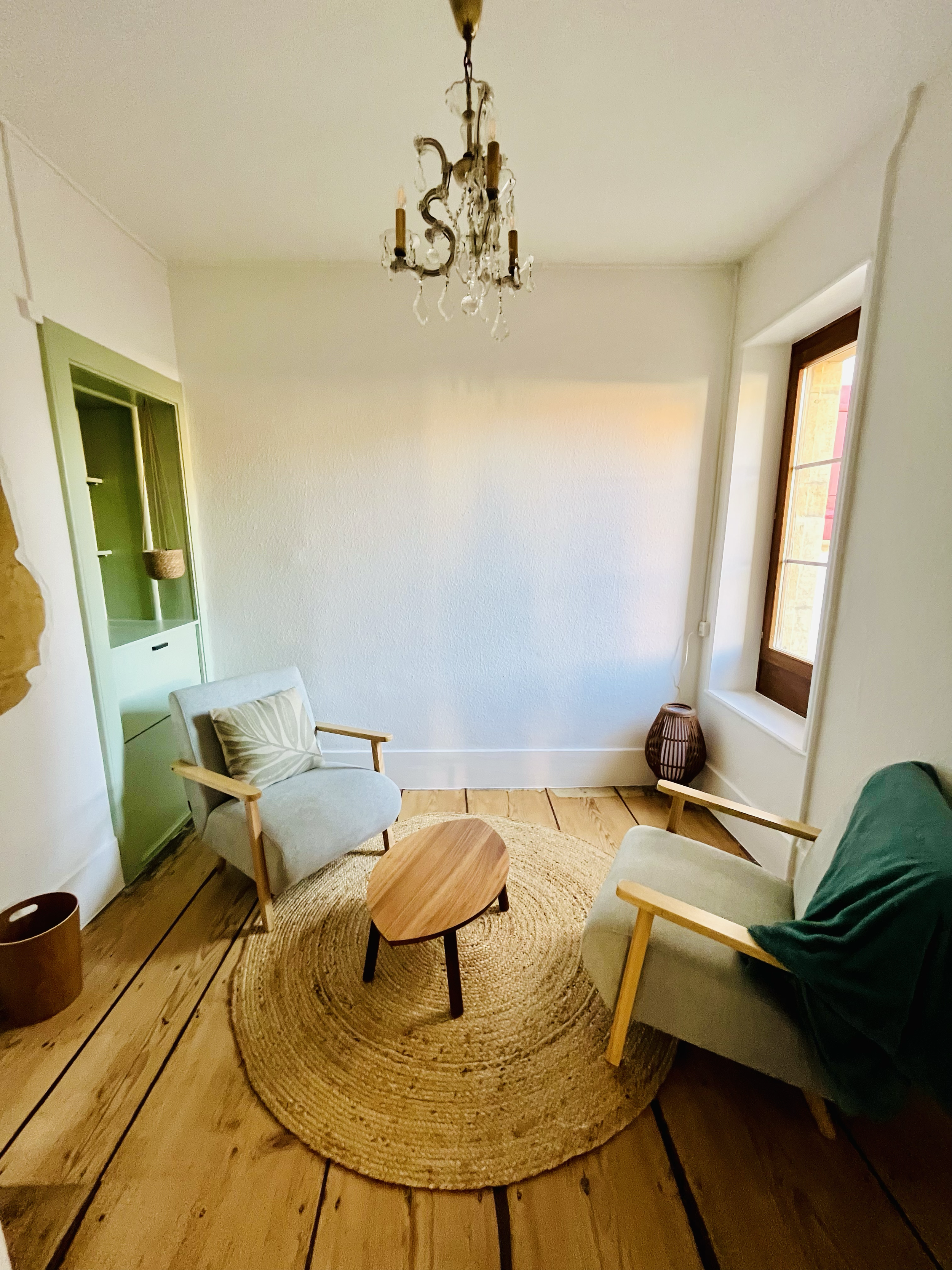 Salon avec deux fauteuils en tissu, un tapis rond en jute, une table en bois, une fenêtre avec un cadre en bois, un chandelier suspendu, décorations de style vintage.