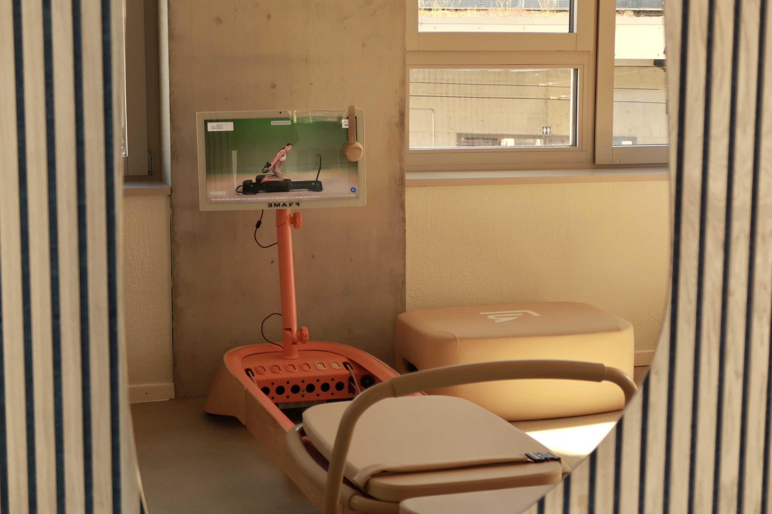 Pilates reformer machine standing in a pilates studio. It's visible in a mirror that is handing on a wall with sound pannels