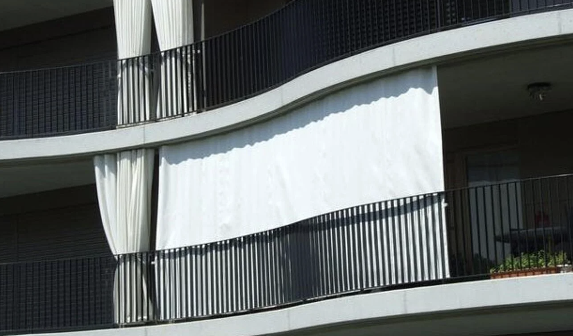 Mehrstöckiges Gebäude mit schwarzen Geländern und weißen Vorhängen auf den Balkons.