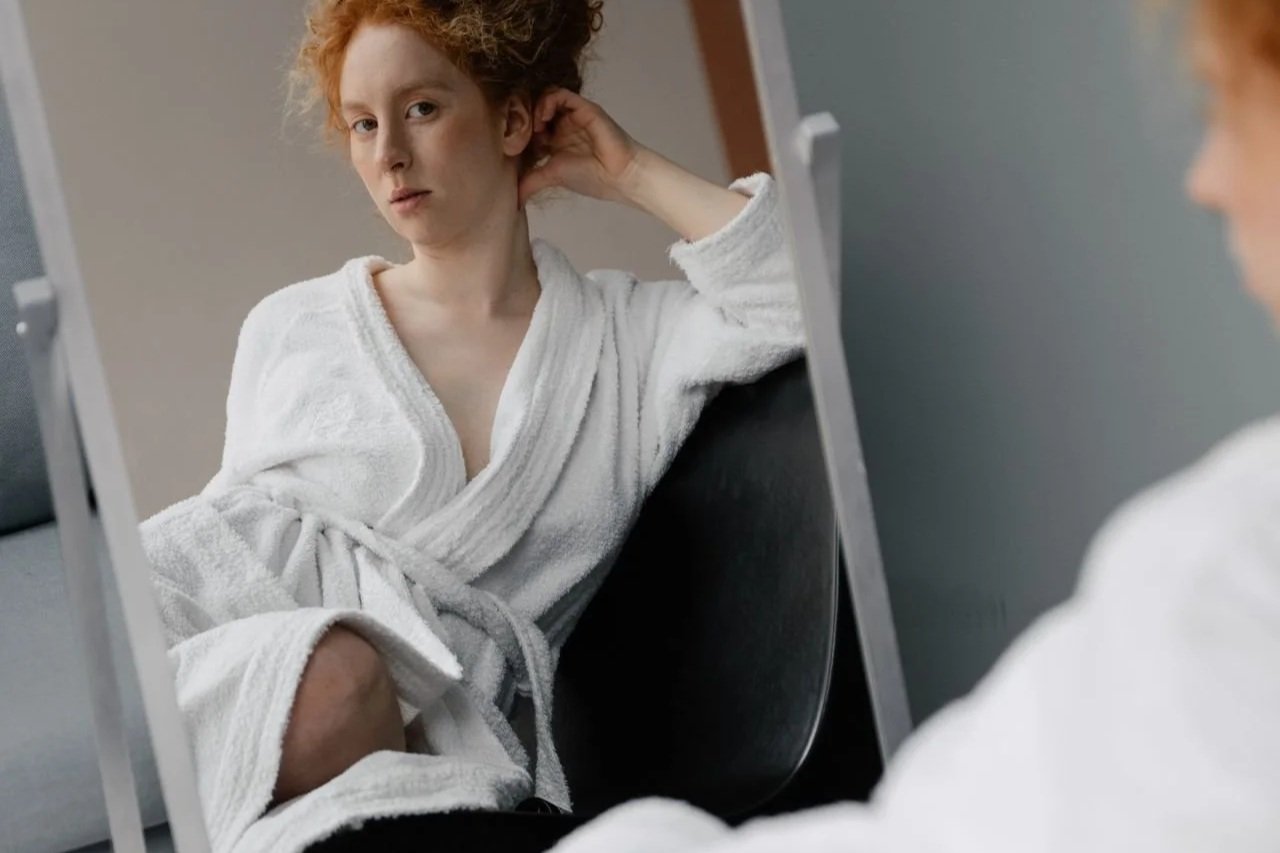 Woman in a robe looking at her body in a mirror