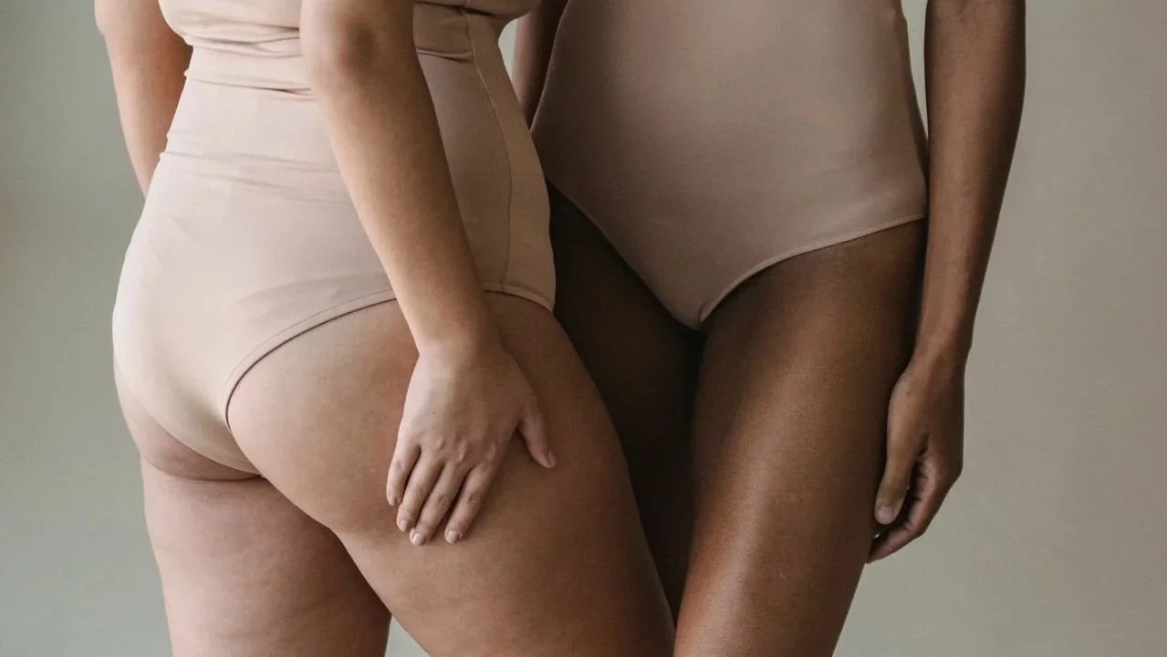 Two women wearing beige bodysuits