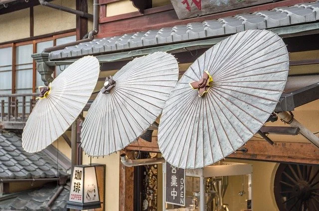 Trois parasols en papier blanc suspendus devant un bâtiment traditionnel japonais.