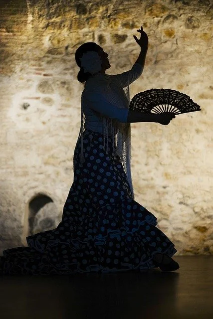 Silhouette d'une femme qui danse, tenant un éventail, dans un lieu avec un mur en pierre en arrière-plan.