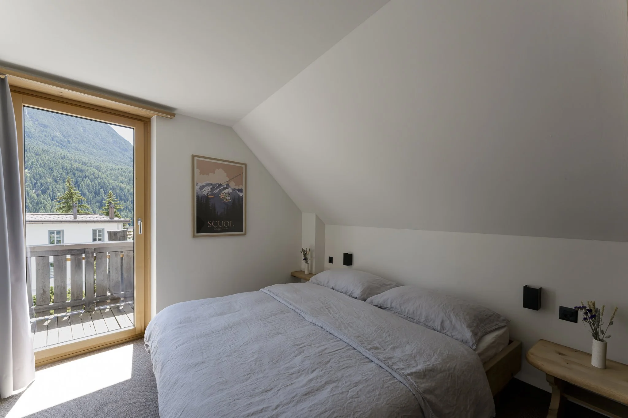 A bedroom with a bed, two bedside tables, and a window with a view of a mountain and trees.
