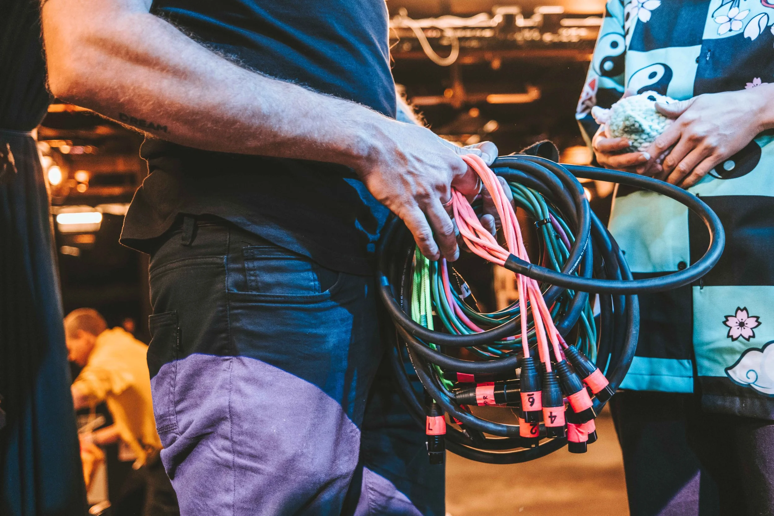 Person hält ein Bündel bunter Kabel hinter der Bühne.