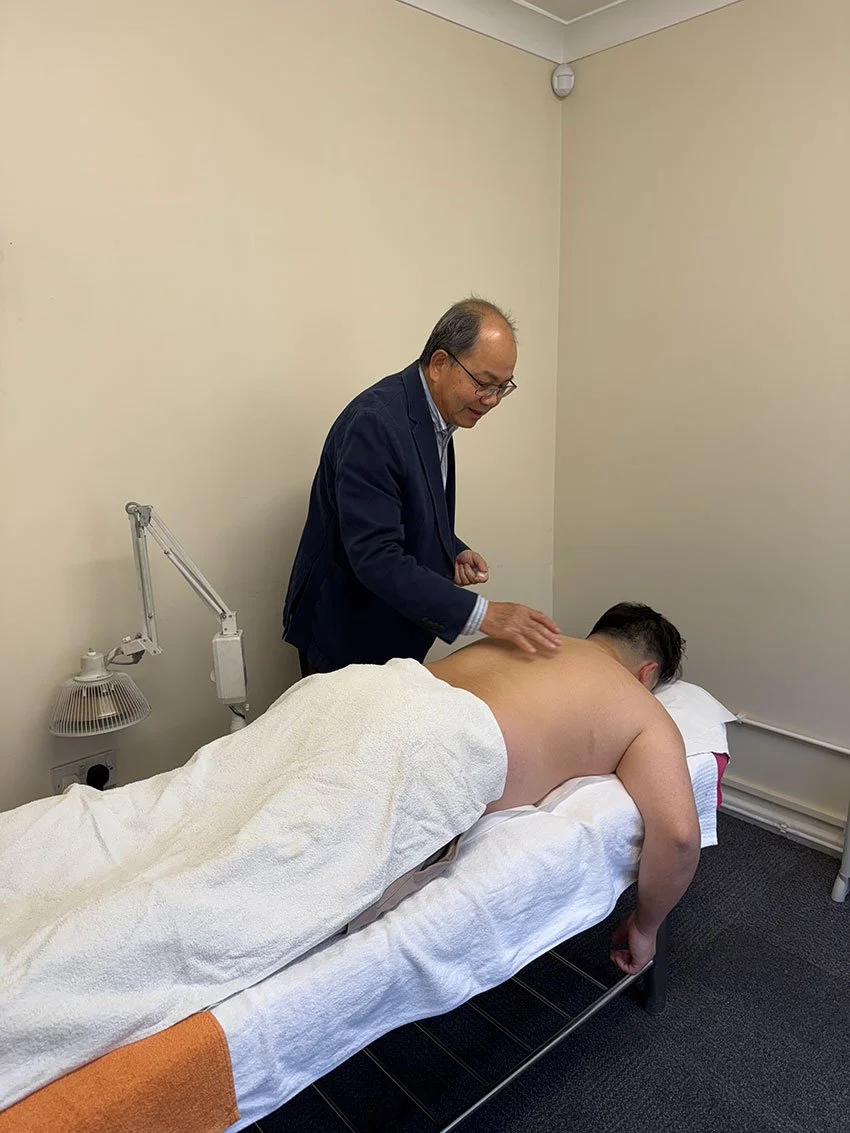 A chiropractor or massage therapist is giving a back massage to a shirtless man lying face down on a treatment table in a clinical setting.