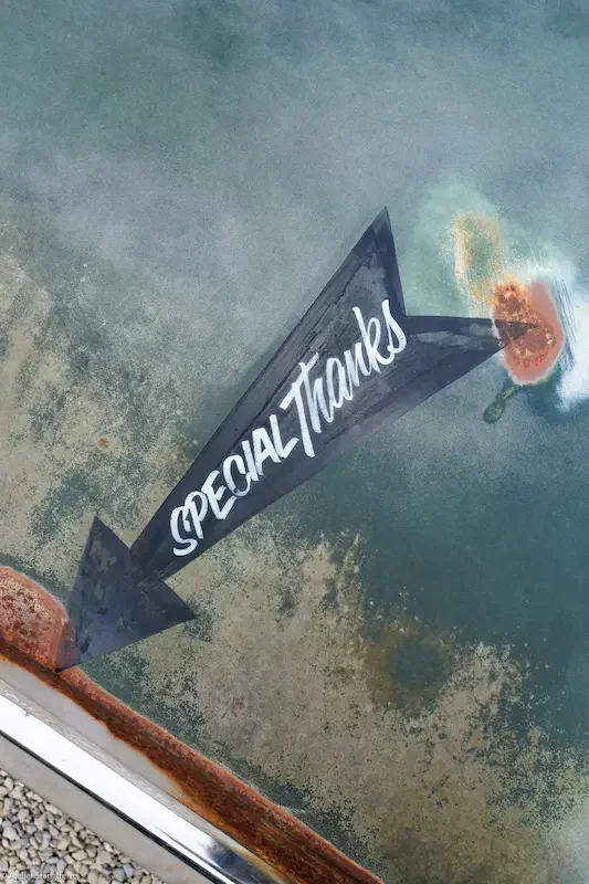 Décoration peinte en forme de flèche indiquant «Special Thanks» sur une carrosserie de voiture, avec des marques de rouille et une surface légèrement usée.