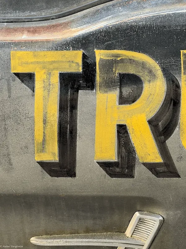 Lettre peint en jaune sur une surface sombre, partiellement visible