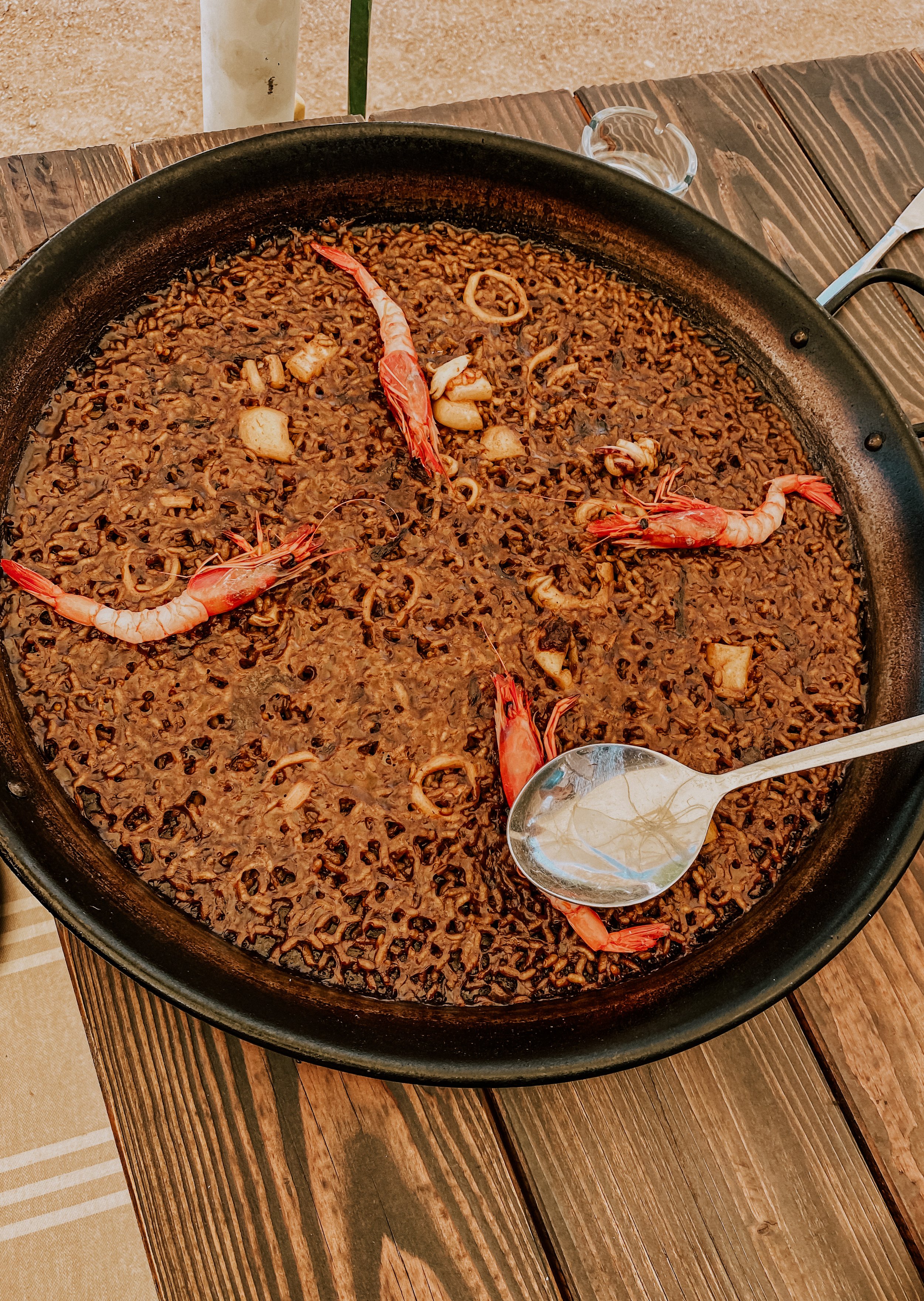 Traditional Spanish fideuà with seafood, including shrimp and cuttlefish, in a wide black pan on a wooden table.