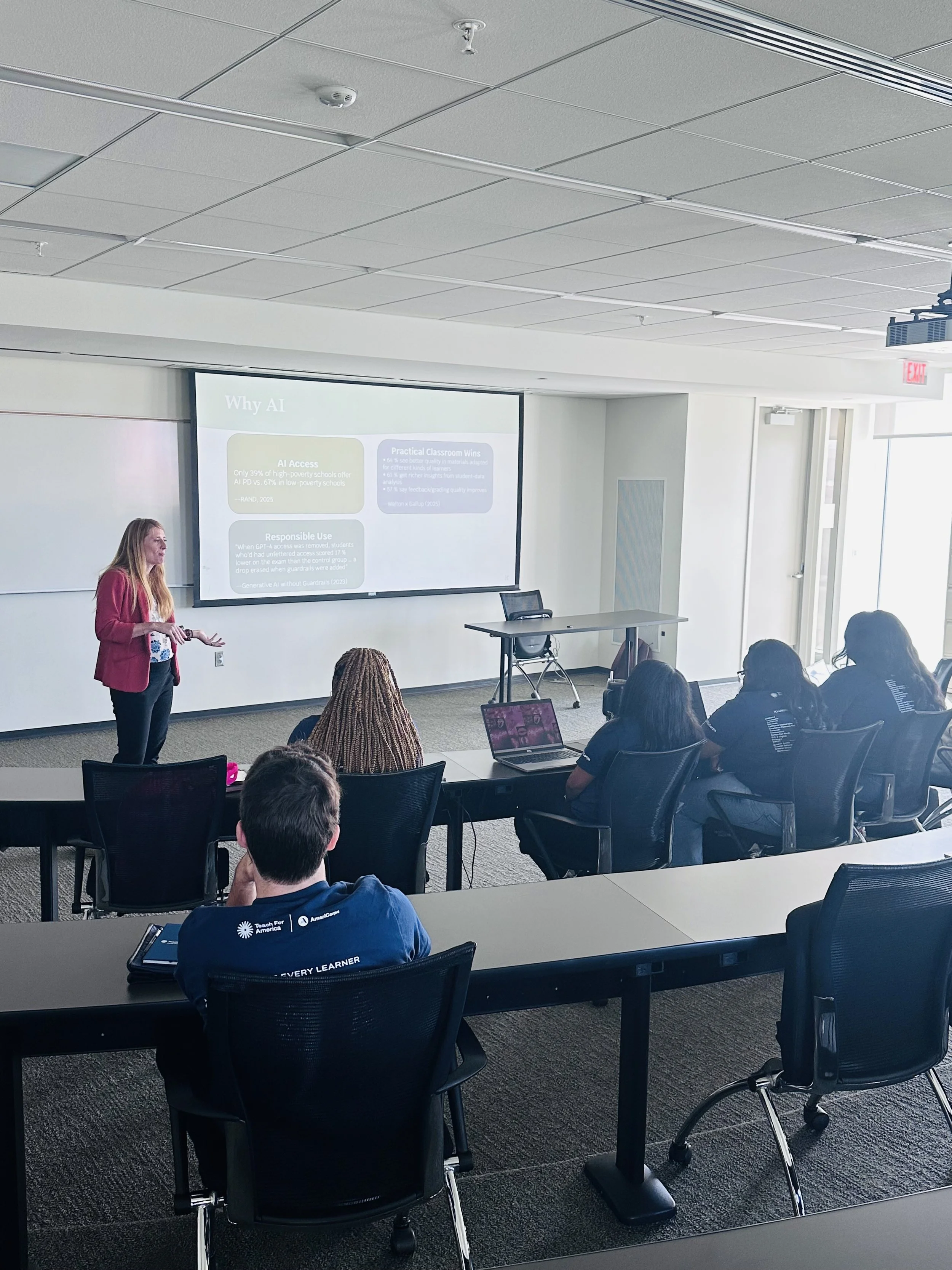 A woman presenting in a classroom or conference room with a slide titled 'Why AI' projected on a screen behind her. The audience, seated at tables with laptops and notebooks, listens attentively.