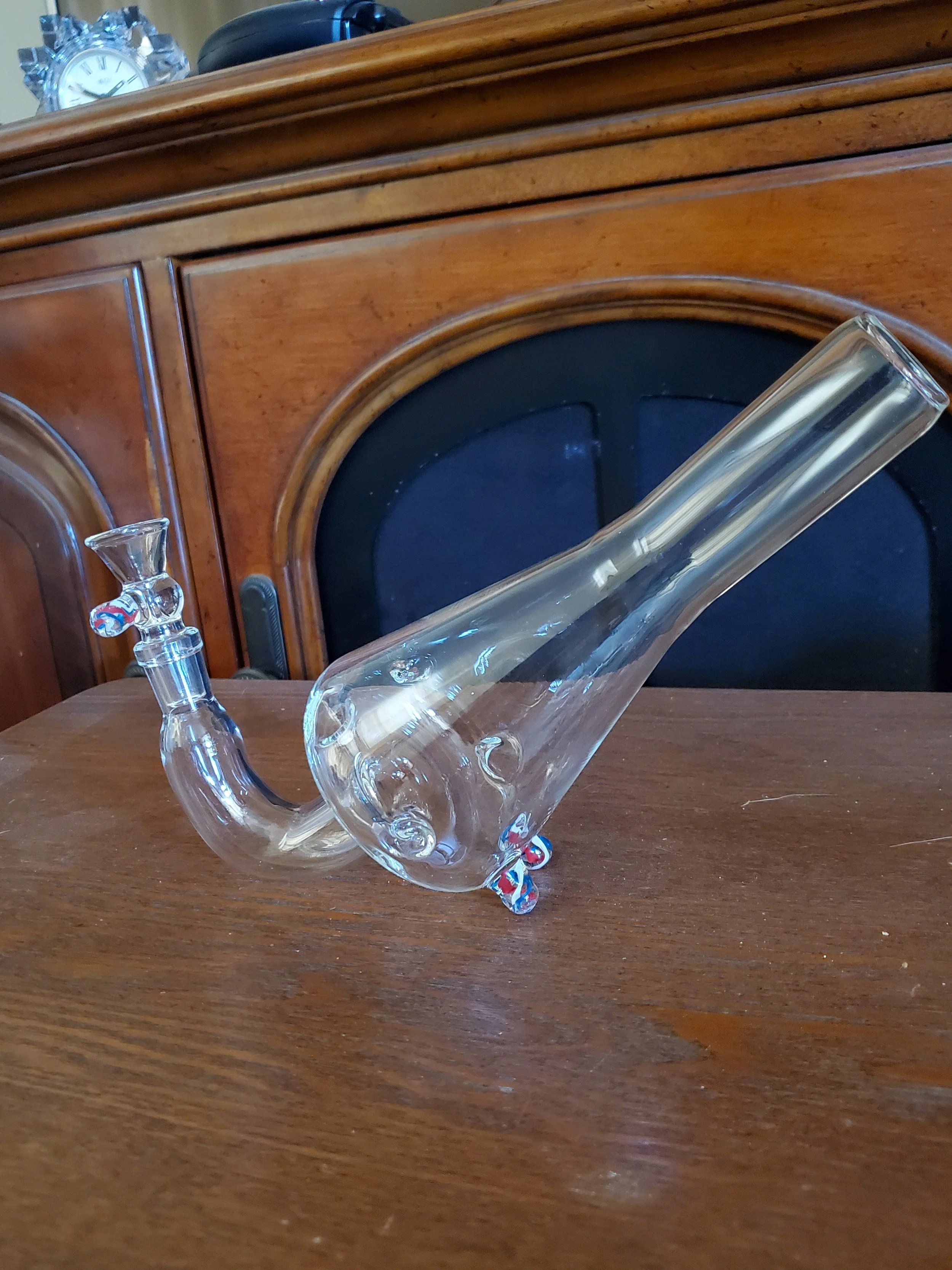 Glass smoking pipe with a curved neck and decorative foot pieces on a wooden surface.