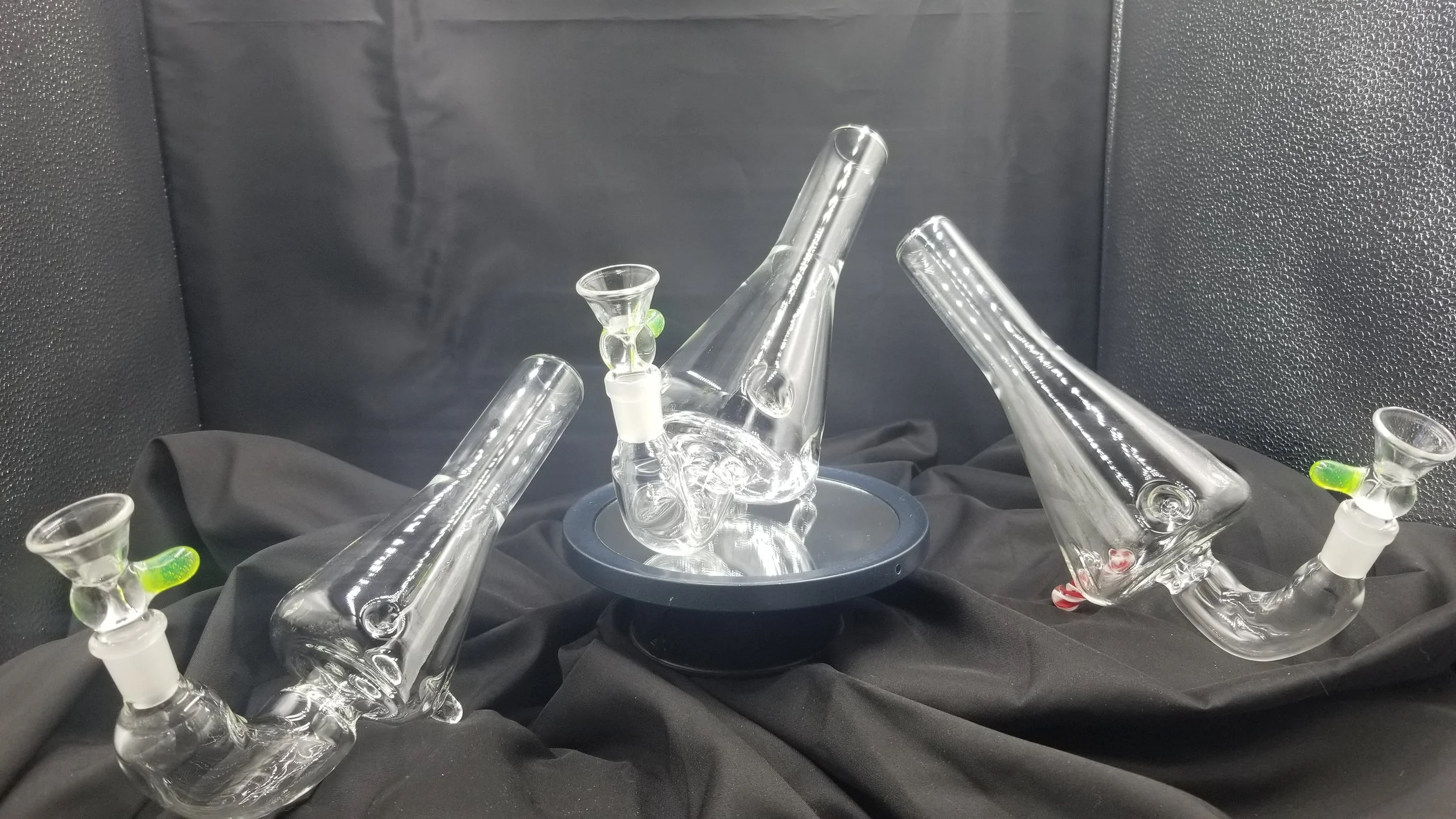 Set of three glass pipes with glass joints, arranged on black fabric with a black textured background.