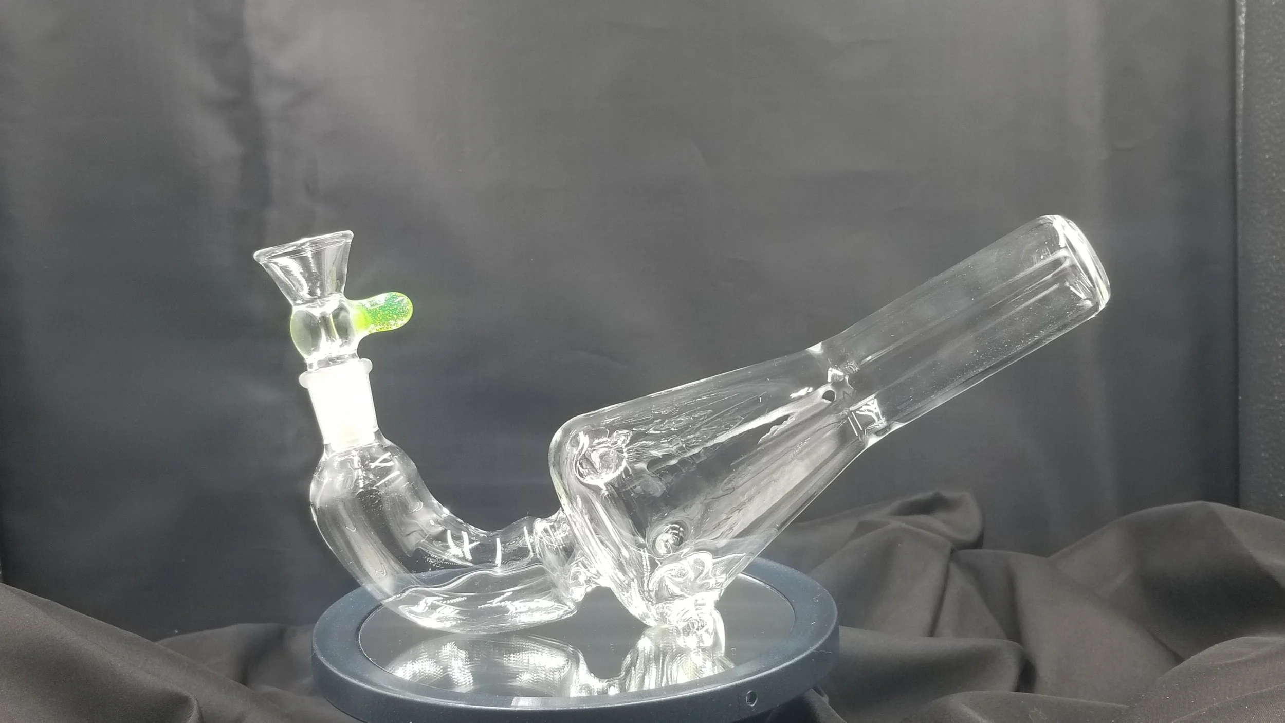 A clear glass bong with a green-colored bowl, placed on a black surface with a black background.