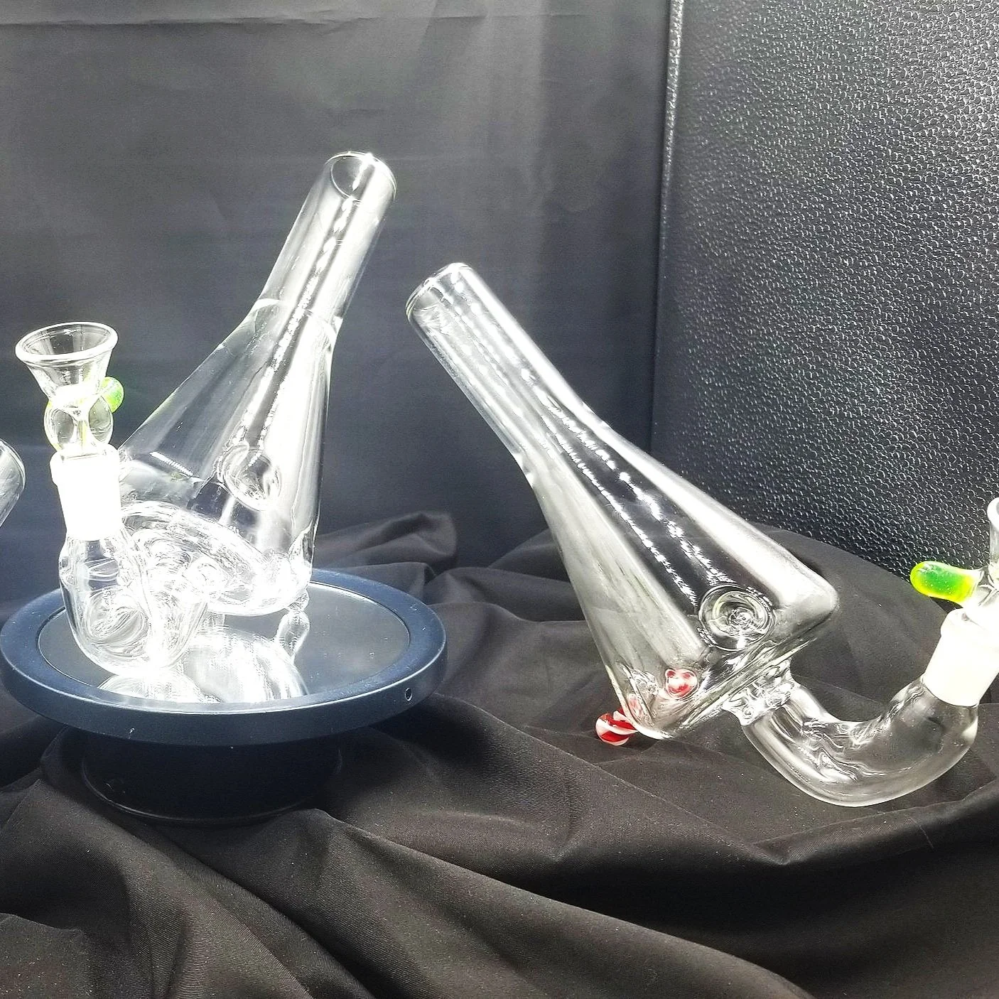 Glass bongs and pipes for smoking display on black fabric background.