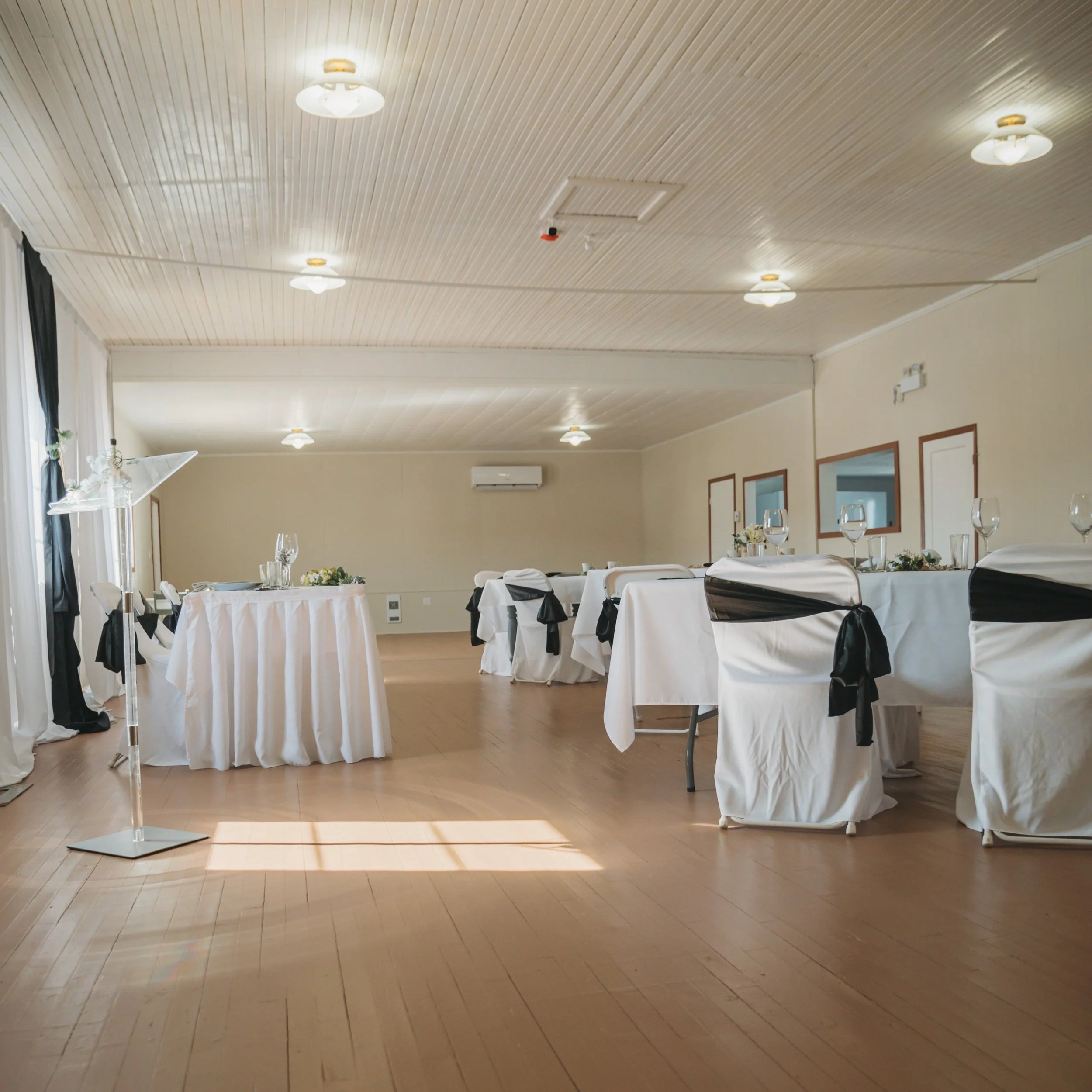 Elegant event space decorated with white tablecloths and black accents, including chair sashes and ribbons, set for a formal event.