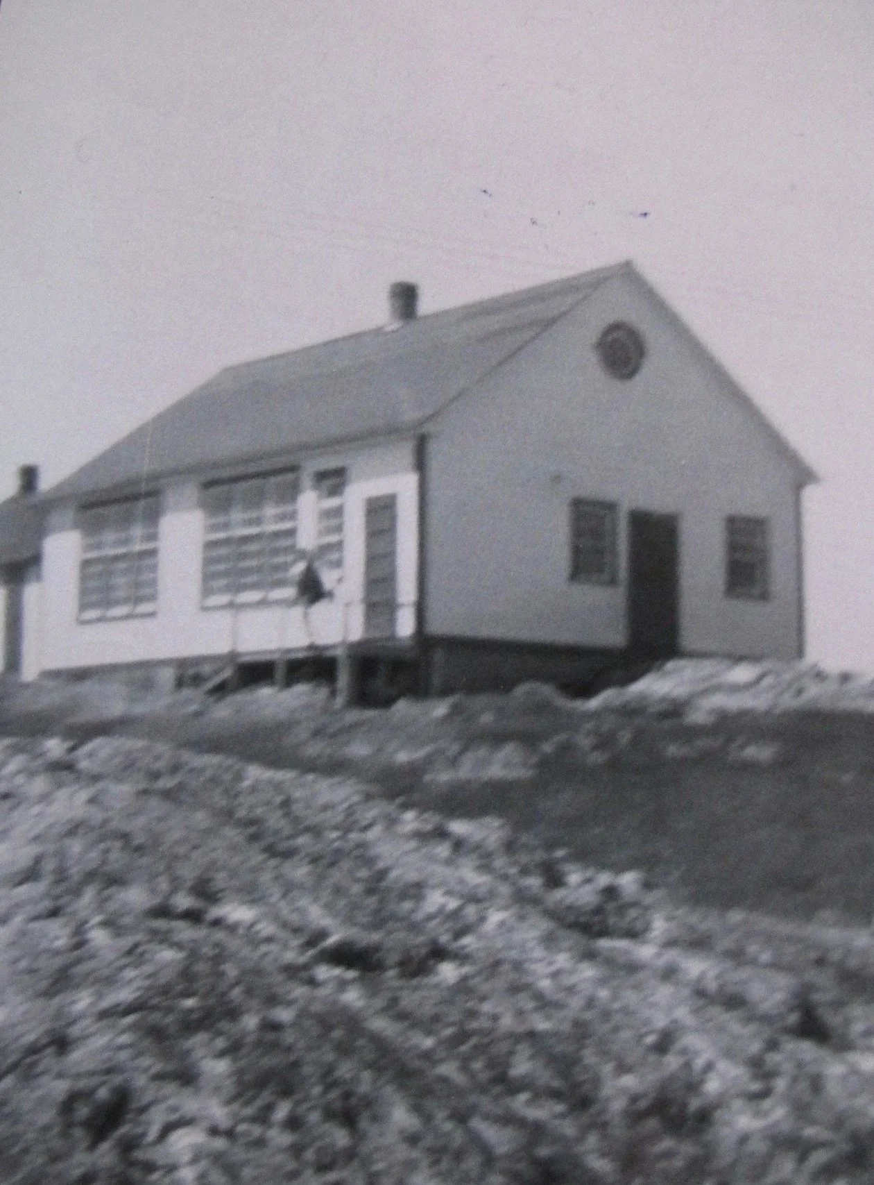Black and white photograph of a building on a rocky, snow-dusted terrain with a clear sky in the background.