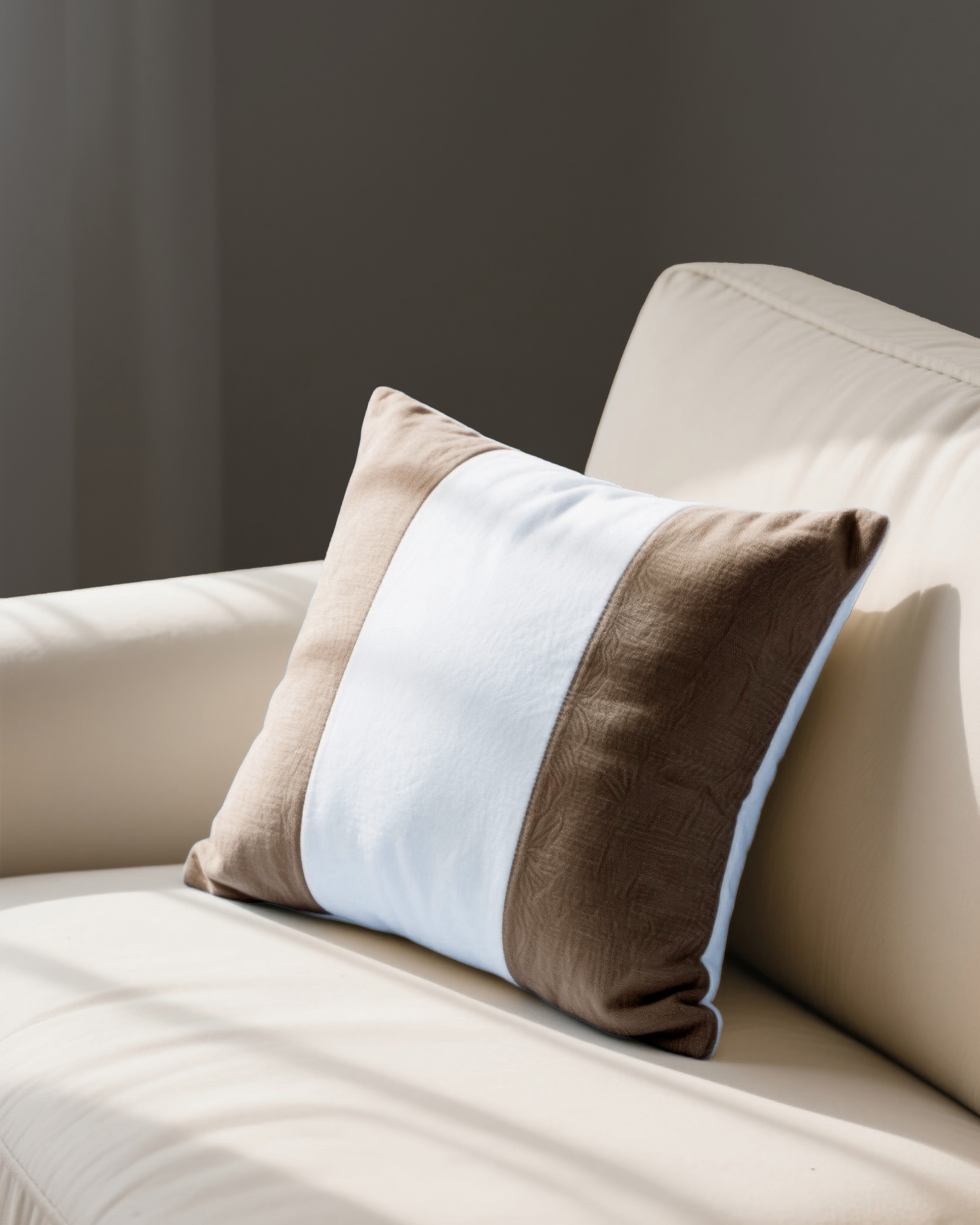 Detailed shot of a luxury cream sofa accented with a minimalist brown and white striped linen throw pillow in natural sunlight.