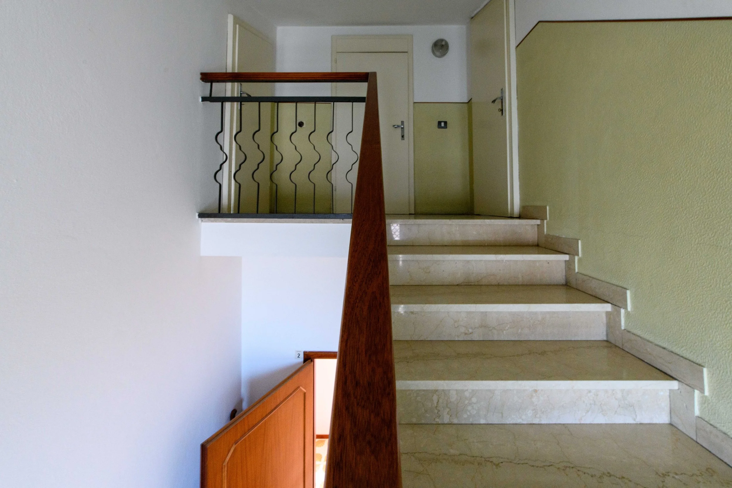 Scala di pietra con corrimano in legno e ferro in un interno di un edificio.