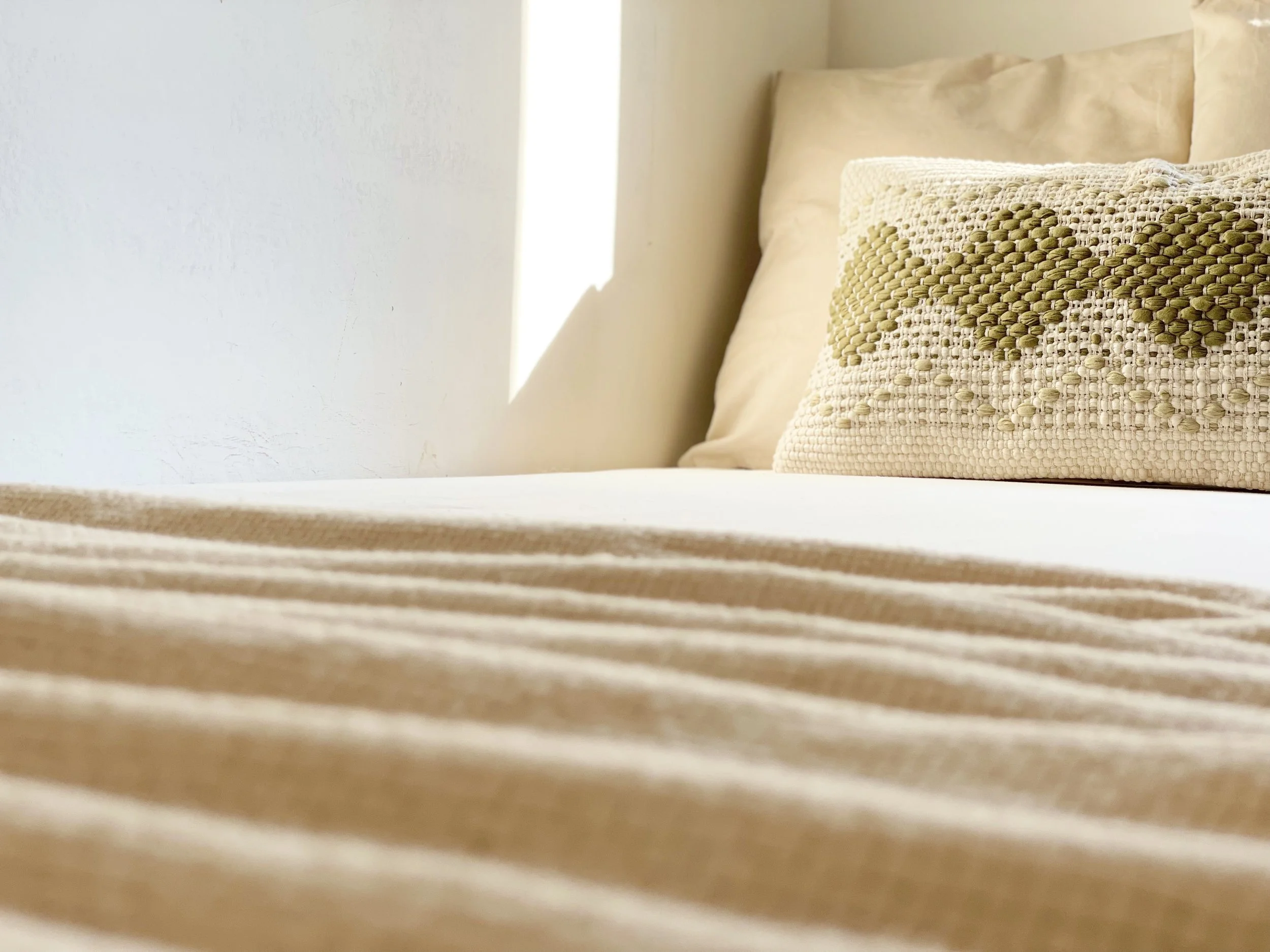 Letto con cuscino decorativo e coperta beige in una stanza luminosa.