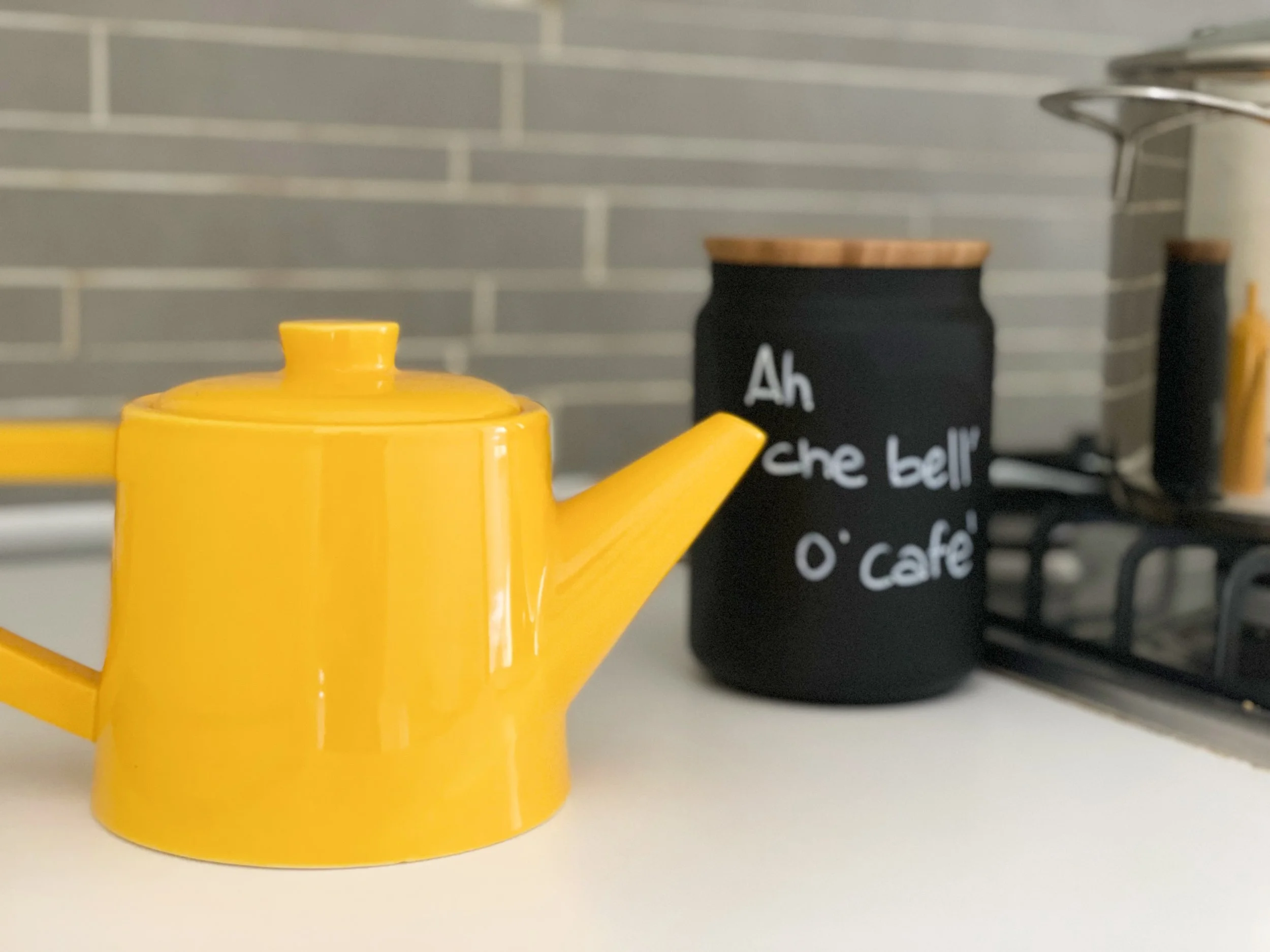Teiera gialla accanto a contenitore con scritta "Ah che bell'o café" su un piano di cucina.