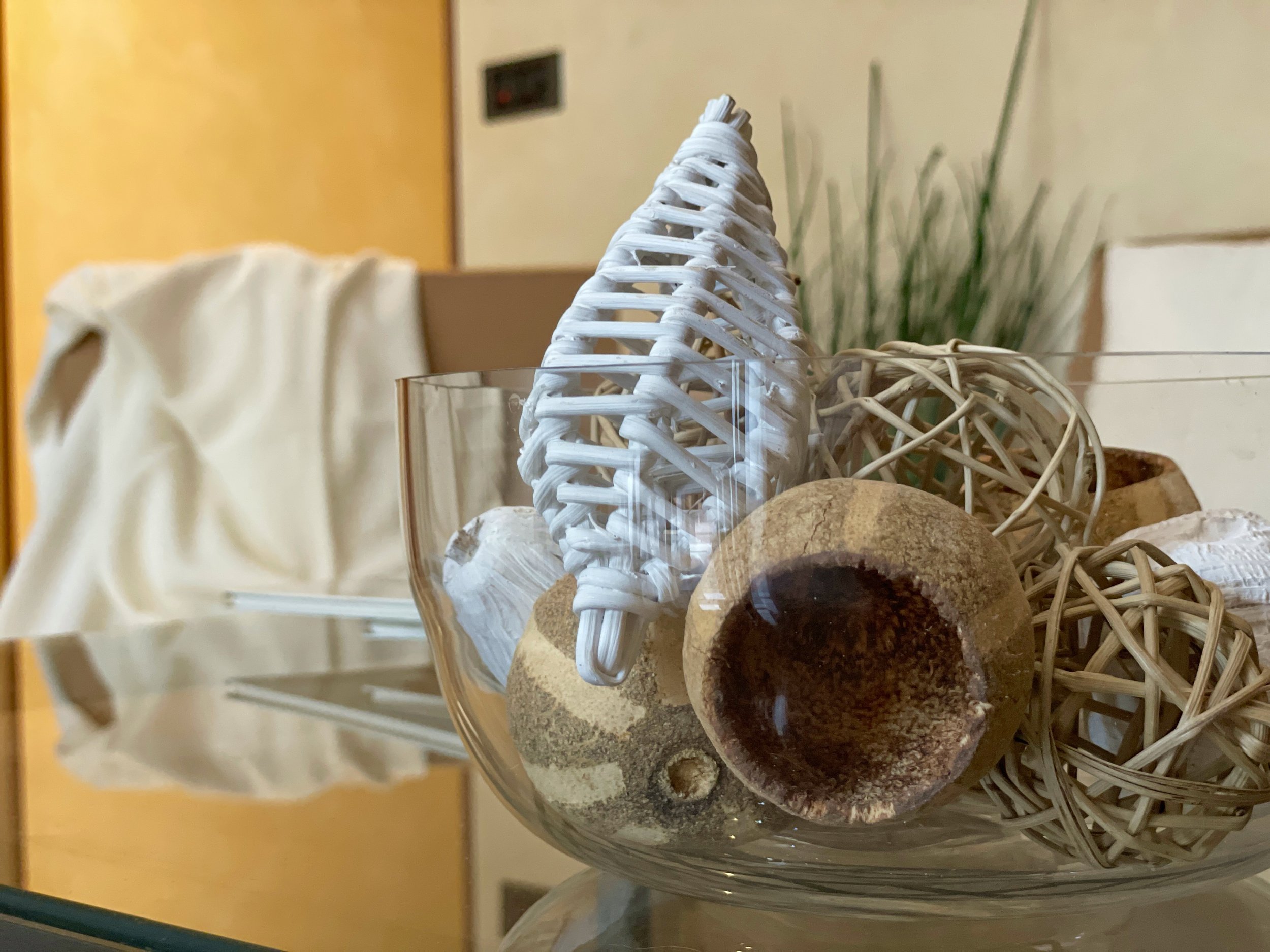 Ciotola di vetro con decorazioni in vimini e legno su un tavolo di vetro, sfondo sfocato di un interno.