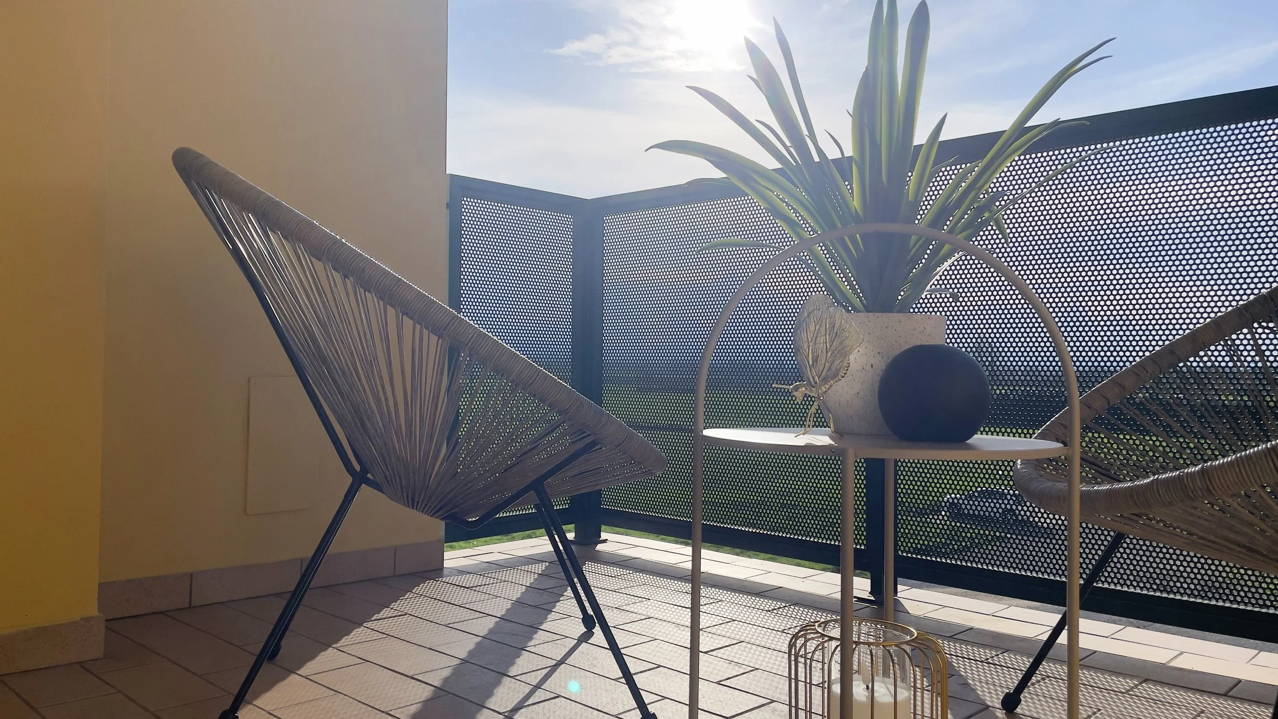Balcone con sedie in stile moderno, tavolino con pianta in vaso e vista esterna soleggiata.
