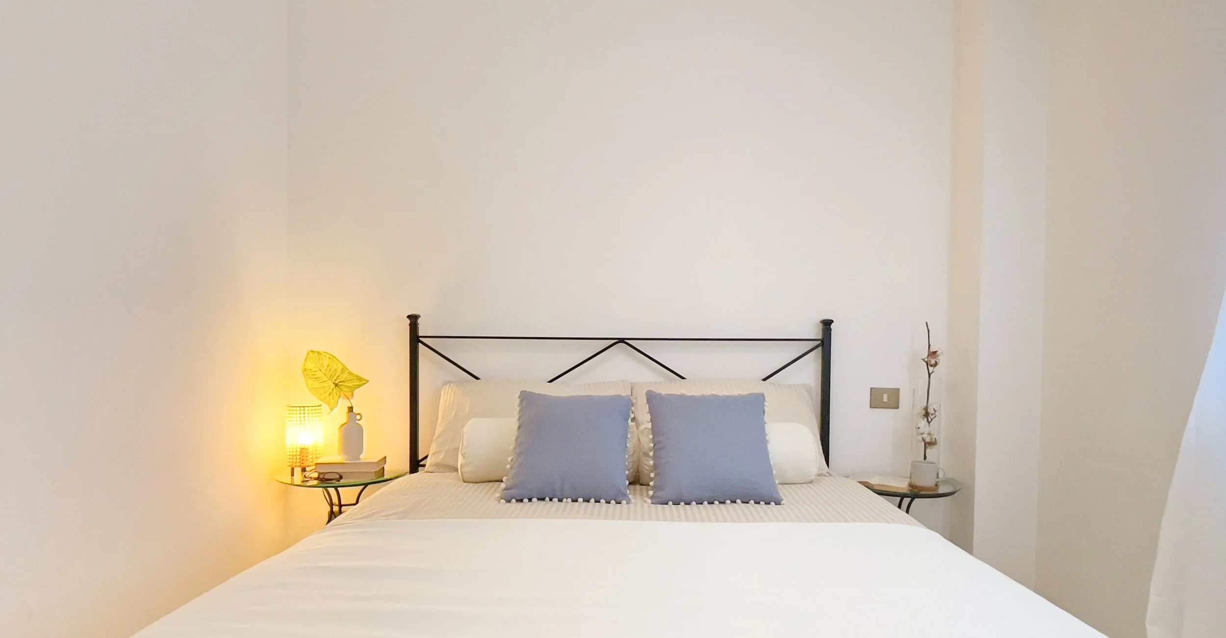 Camera da letto con letto matrimoniale, cuscini blu chiaro, lampada sul comodino e decorazione semplice.