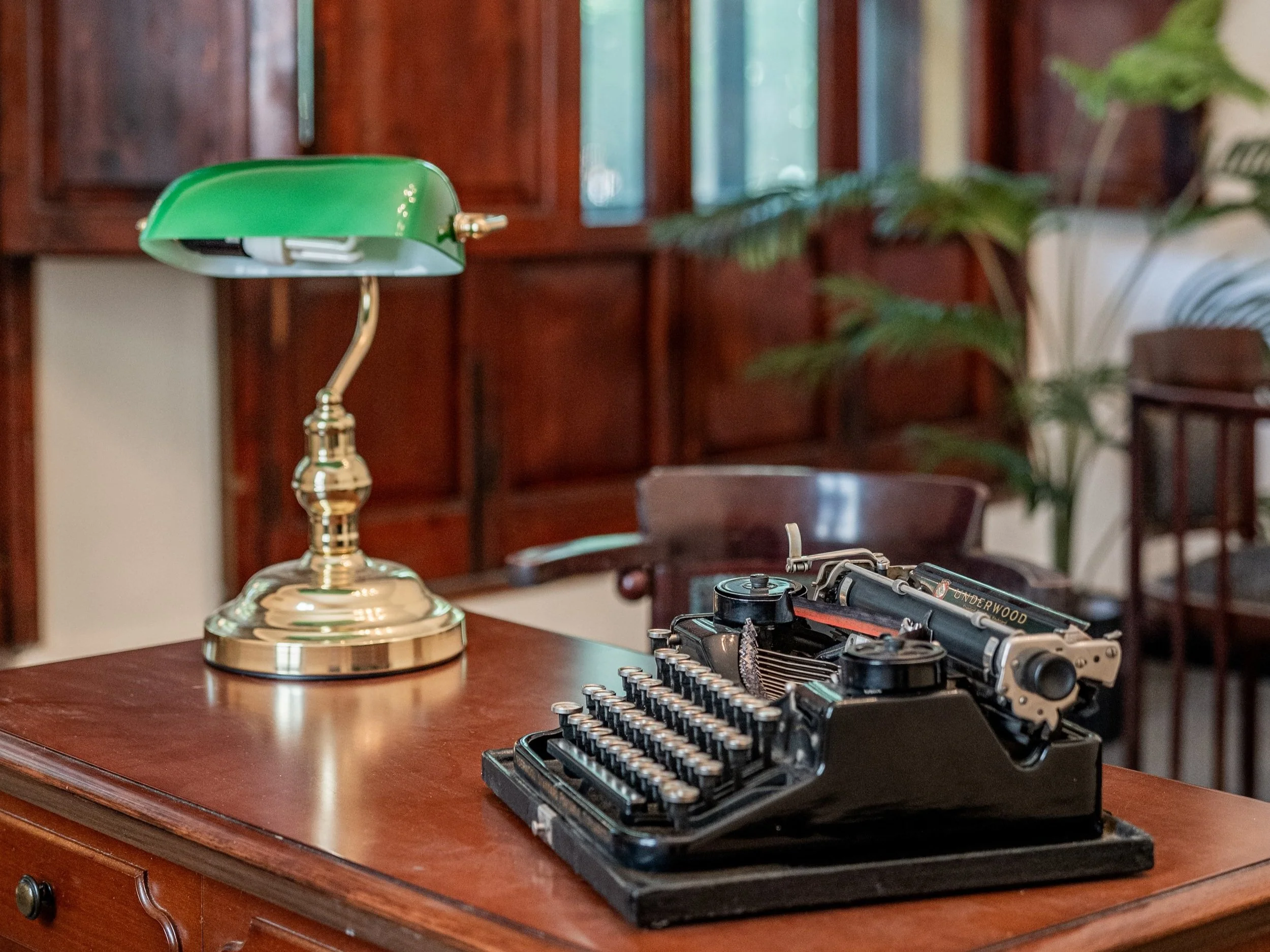 Scrivania in legno con macchina da scrivere vintage e lampada verde in stile retrò.