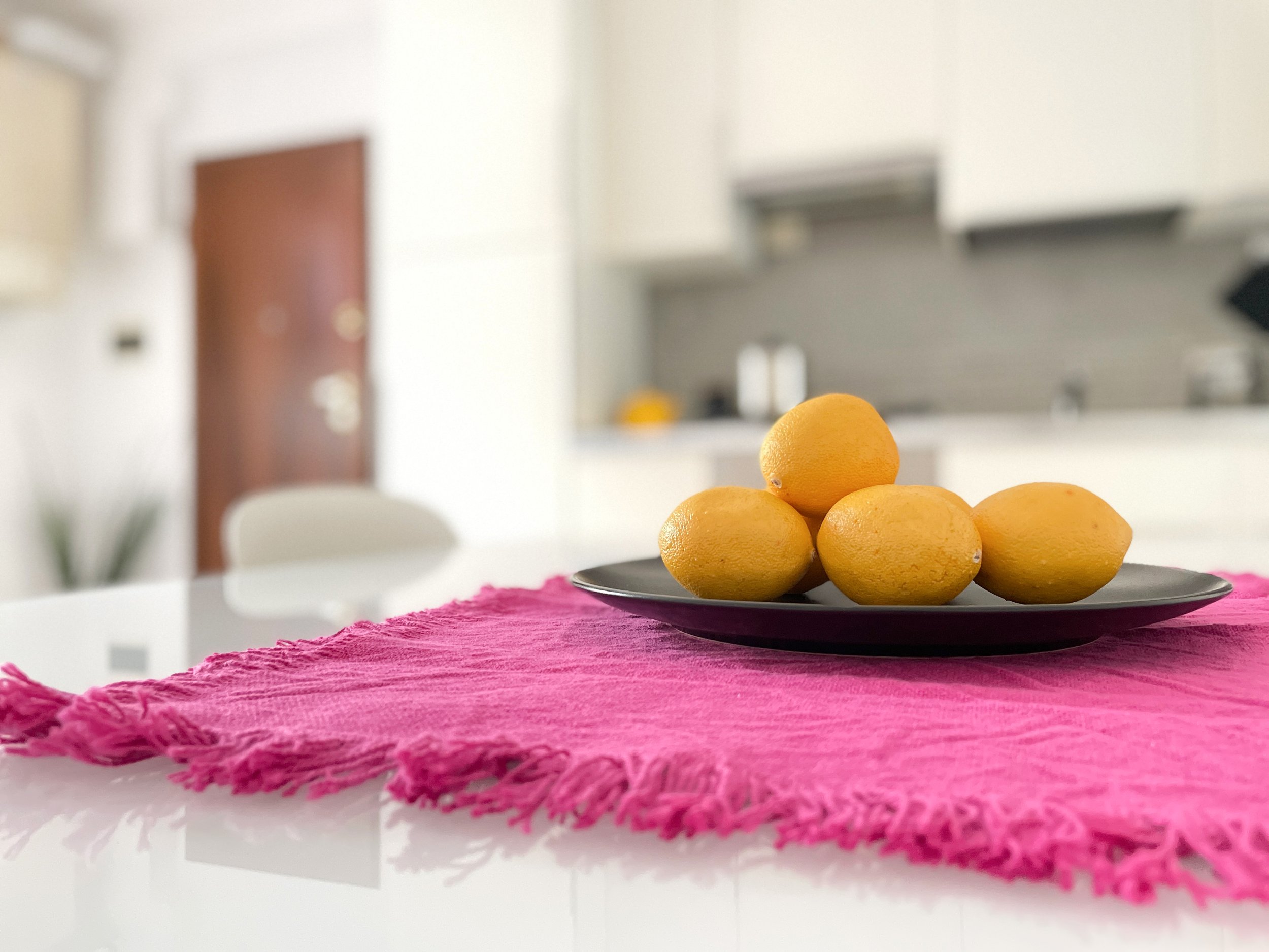 Limoni gialli su un piatto nero su una tovaglia rosa, in una cucina moderna.