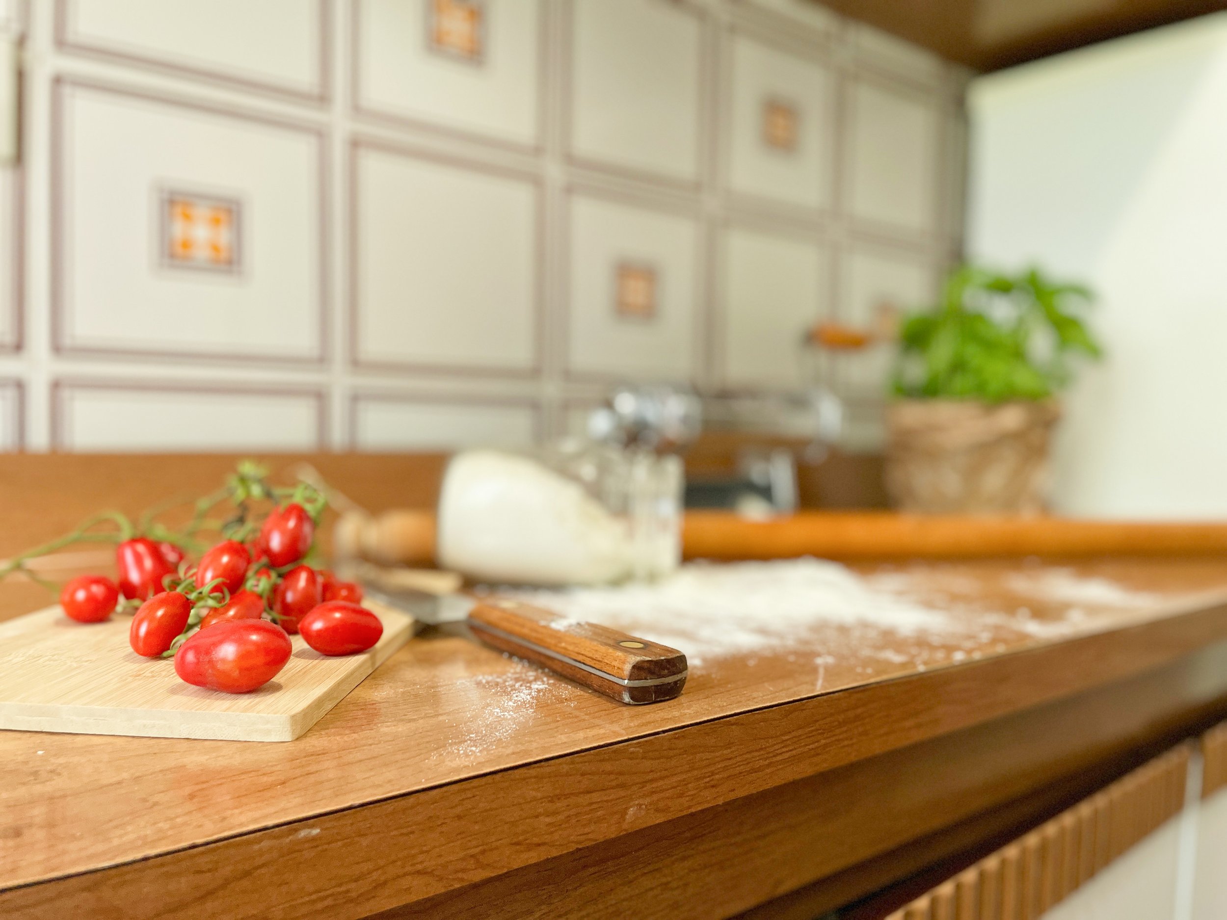 Pomodori su un tagliere di legno in cucina, con farina sparsa e un mattarello sullo sfondo.
