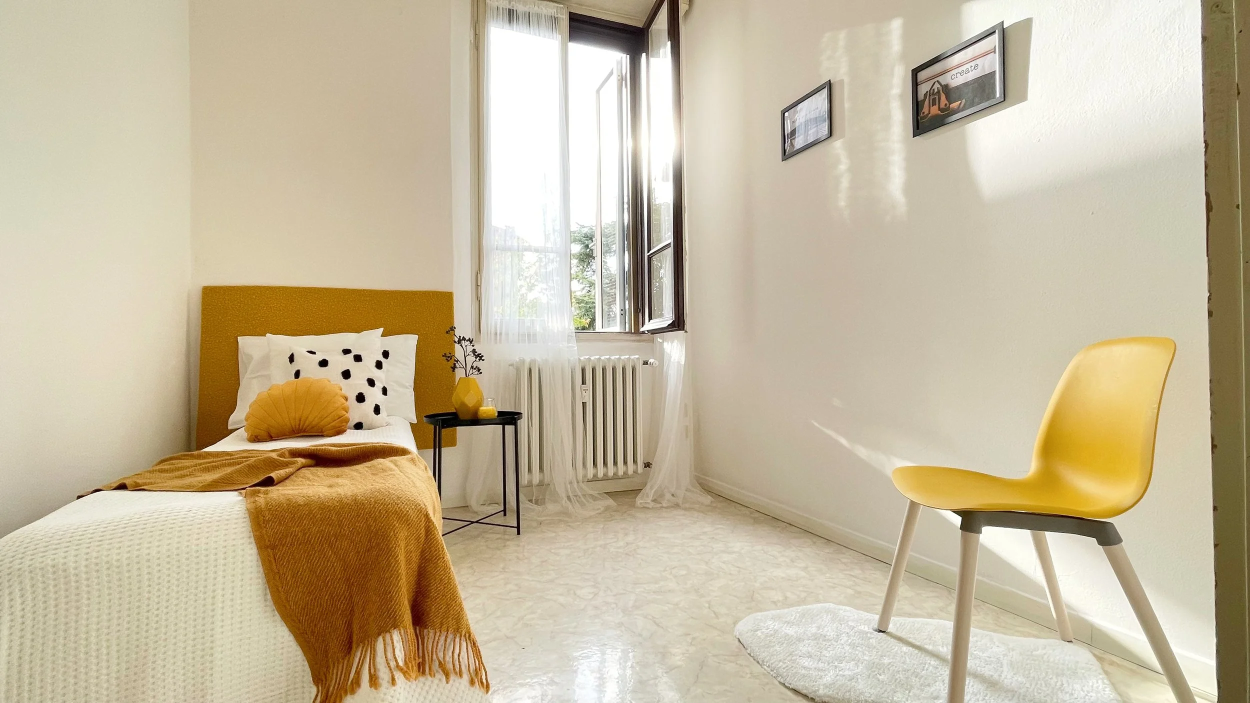 Camera da letto minimalista con letto singolo, coperta gialla, cuscini decorativi, sedia gialla, finestra aperta e decorazioni murali.