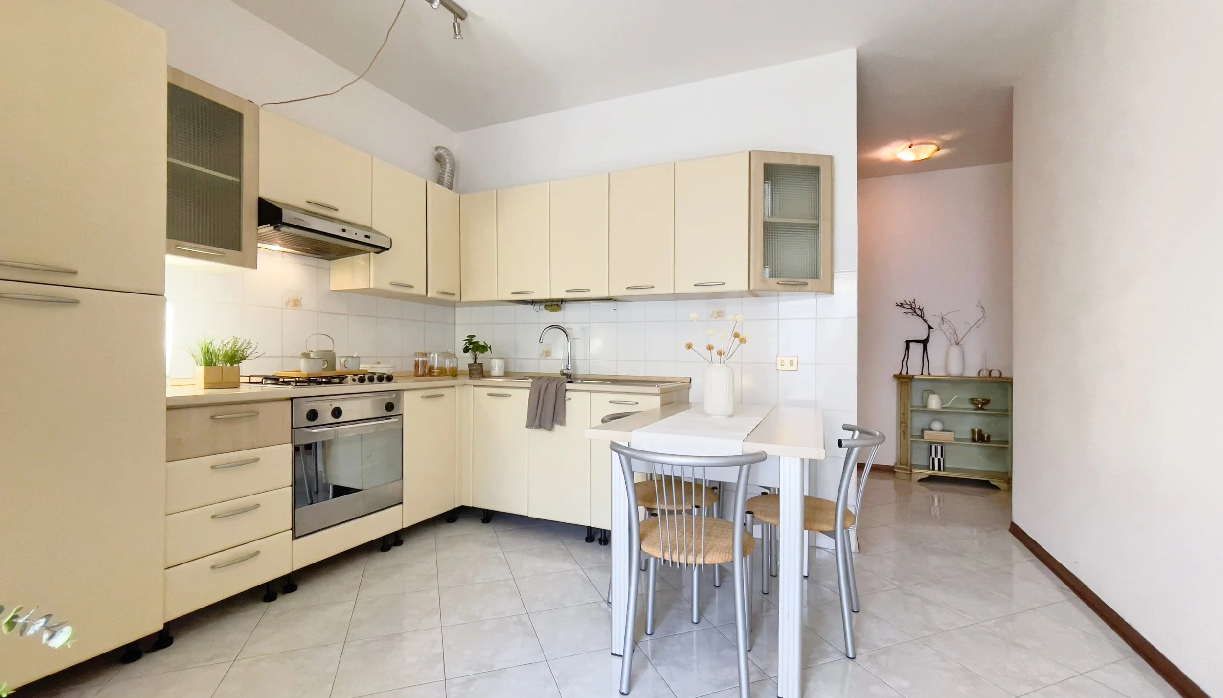 Cucina moderna con mobili chiari, tavolo con sedie, forno e fornelli, decorazioni semplici.