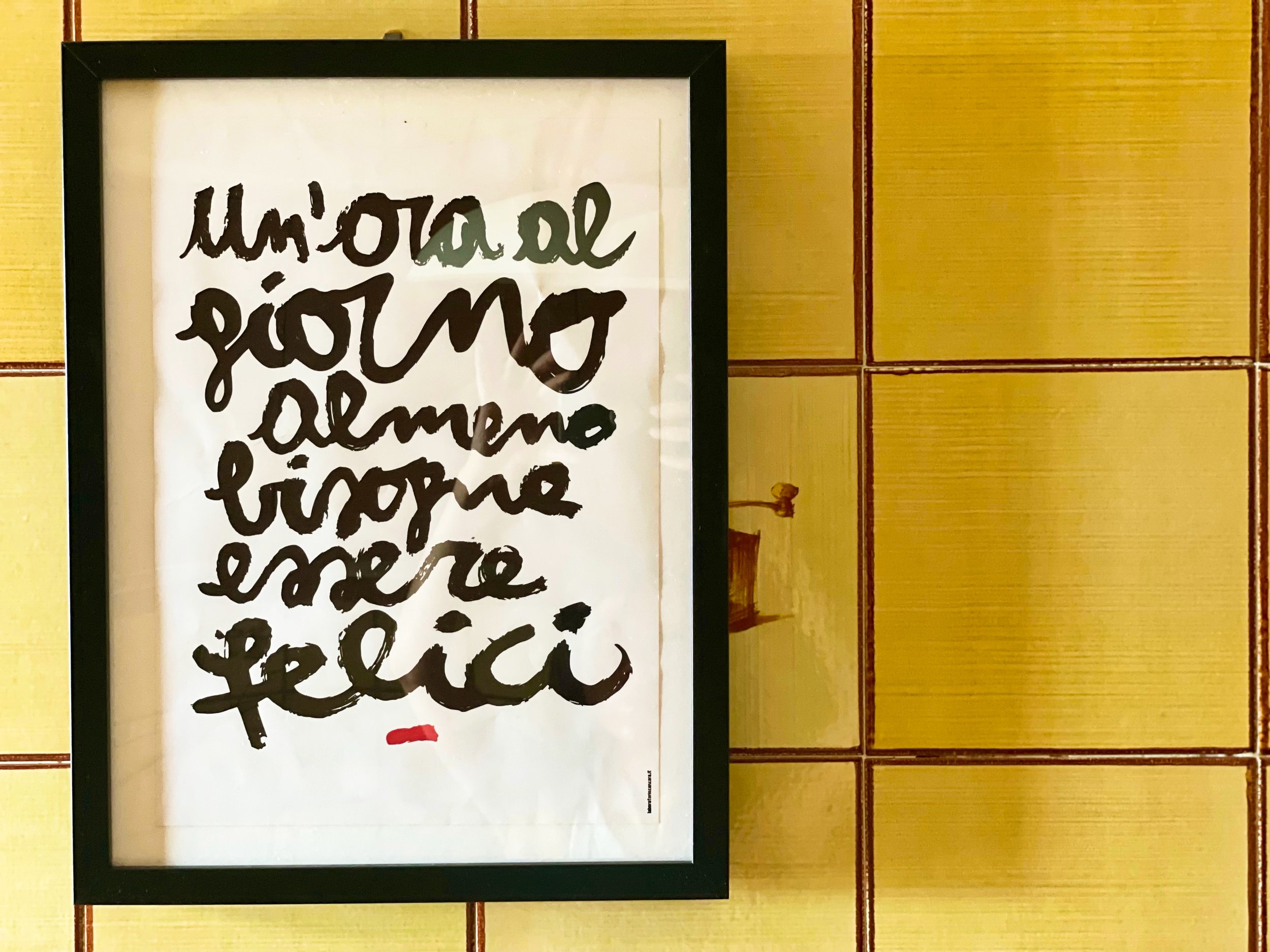 Cornice con citazione "Un'ora al giorno almeno bisogna essere felici" su sfondo di piastrelle gialle.