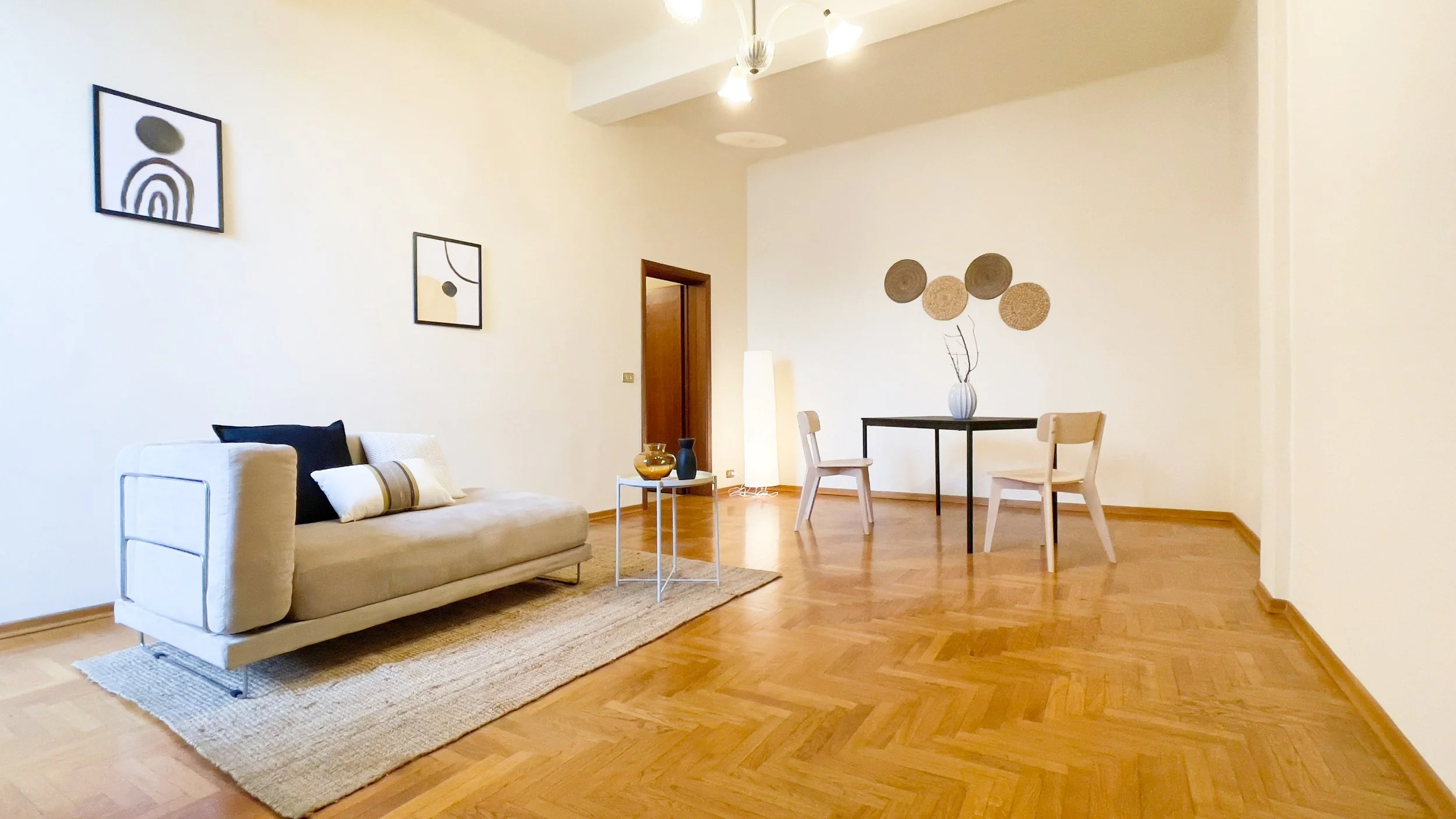 Soggiorno moderno con parquet, divano beige, tavolino bianco, sedie e tavolo nero; decorazioni minimaliste alle pareti.