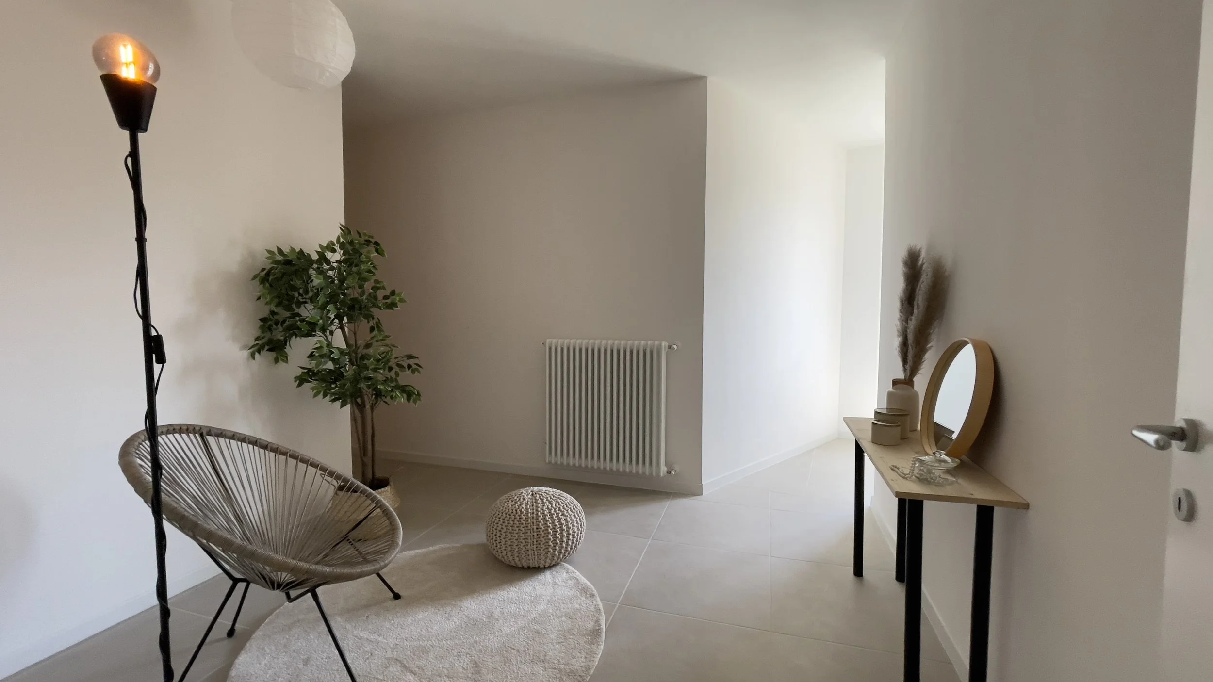 Interno minimalista con sedia moderna, lampada accesa, pianta decorativa, tappeto rotondo e consolle con specchio e decorazioni.
