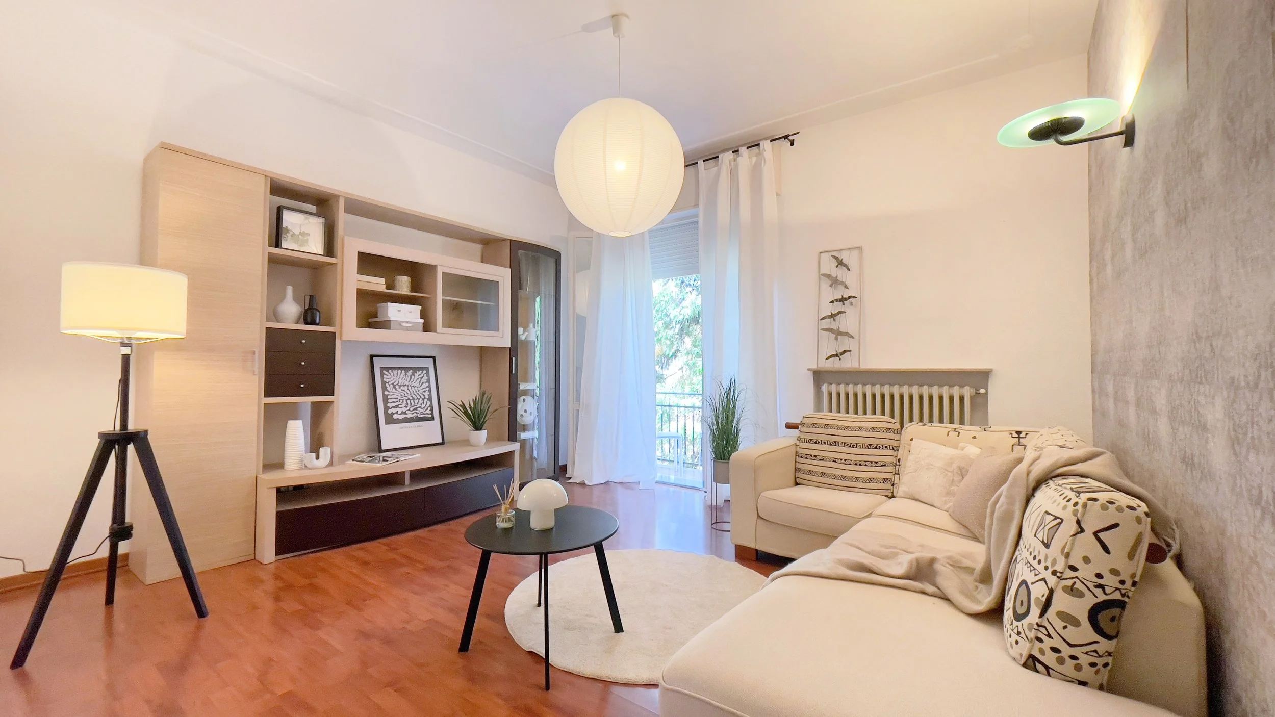 Soggiorno moderno con divano beige, tavolino nero, lampada da terra e libreria con decorazioni.